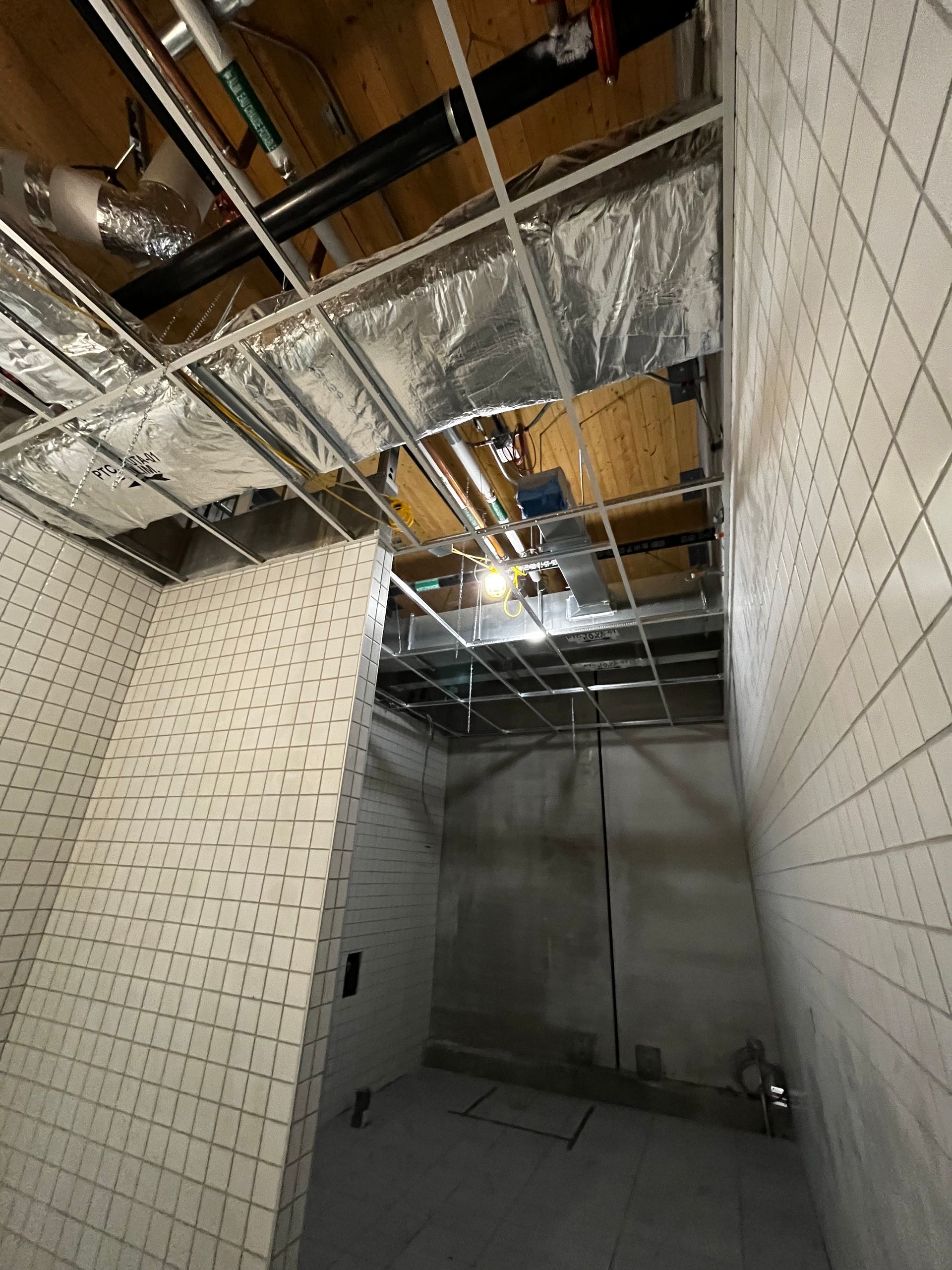 Intérieur d'un chantier de construction avec plafond à ossature apparente, conduits de ventilation et murs carrelés.