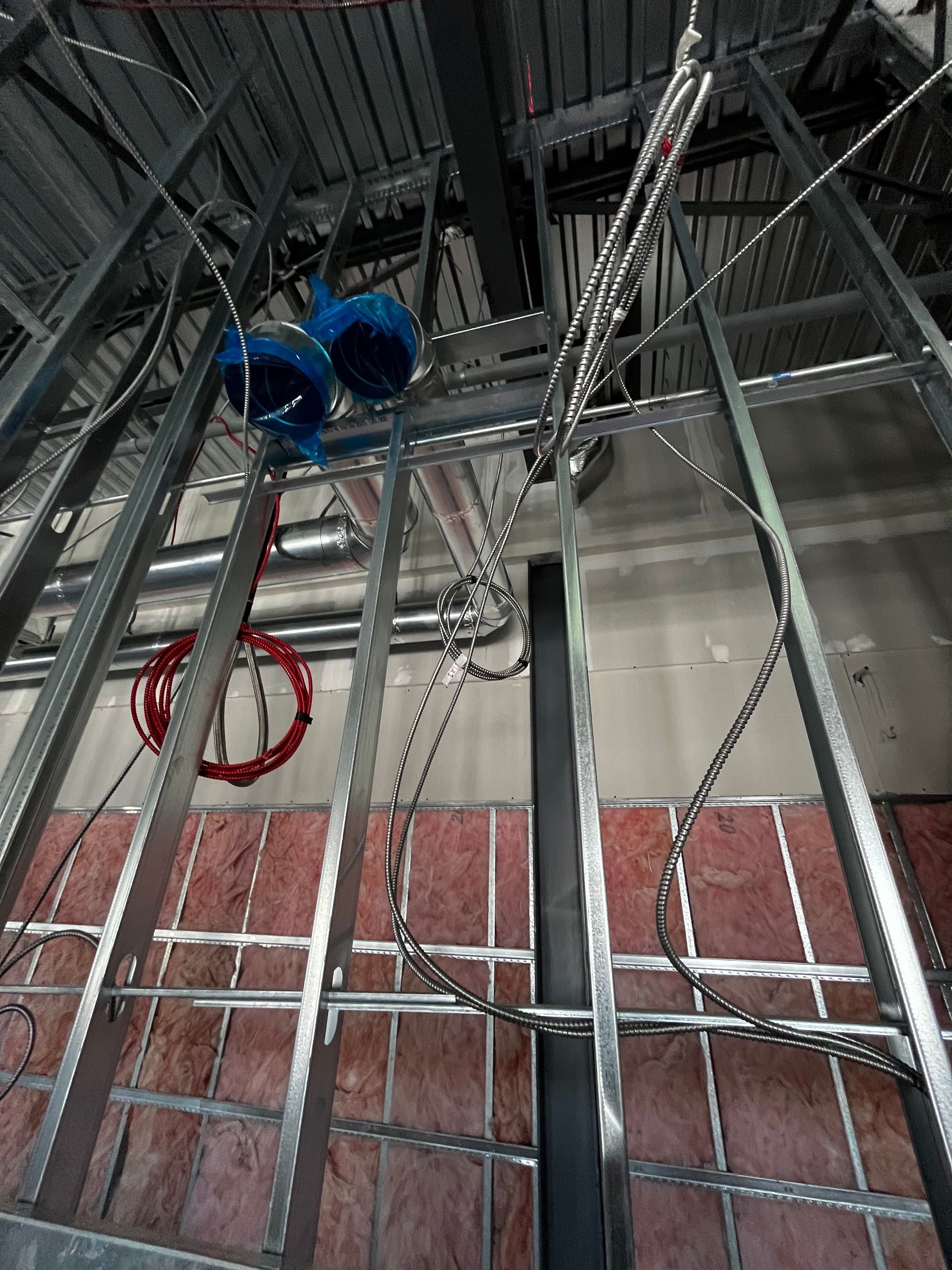 Ossature métallique pour cloison intérieure, avec câbles et tuyauterie apparents.