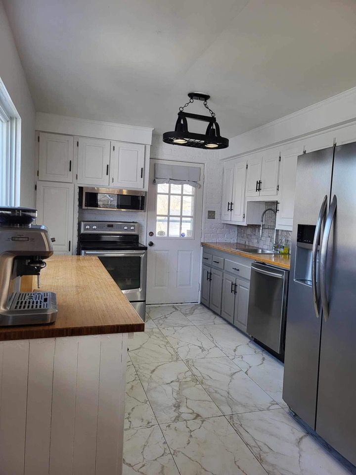 Cuisine avec armoires blanches, appareils électroménagers en acier inoxydable, comptoirs en bois massif et sol carrelé à motifs.