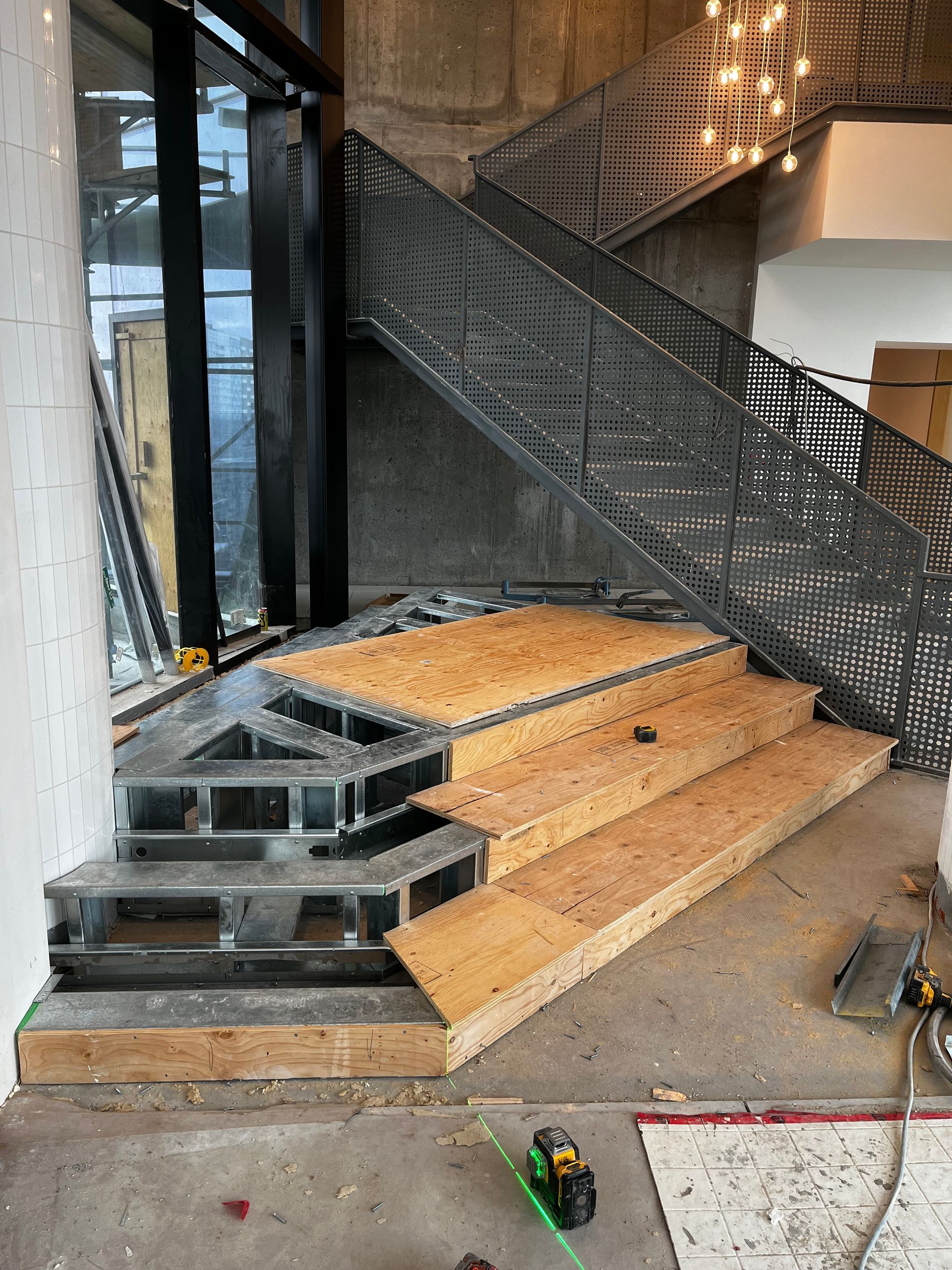 Escalier en construction avec structure métallique et marches en bois. Rambarde en métal gris et mur en béton.