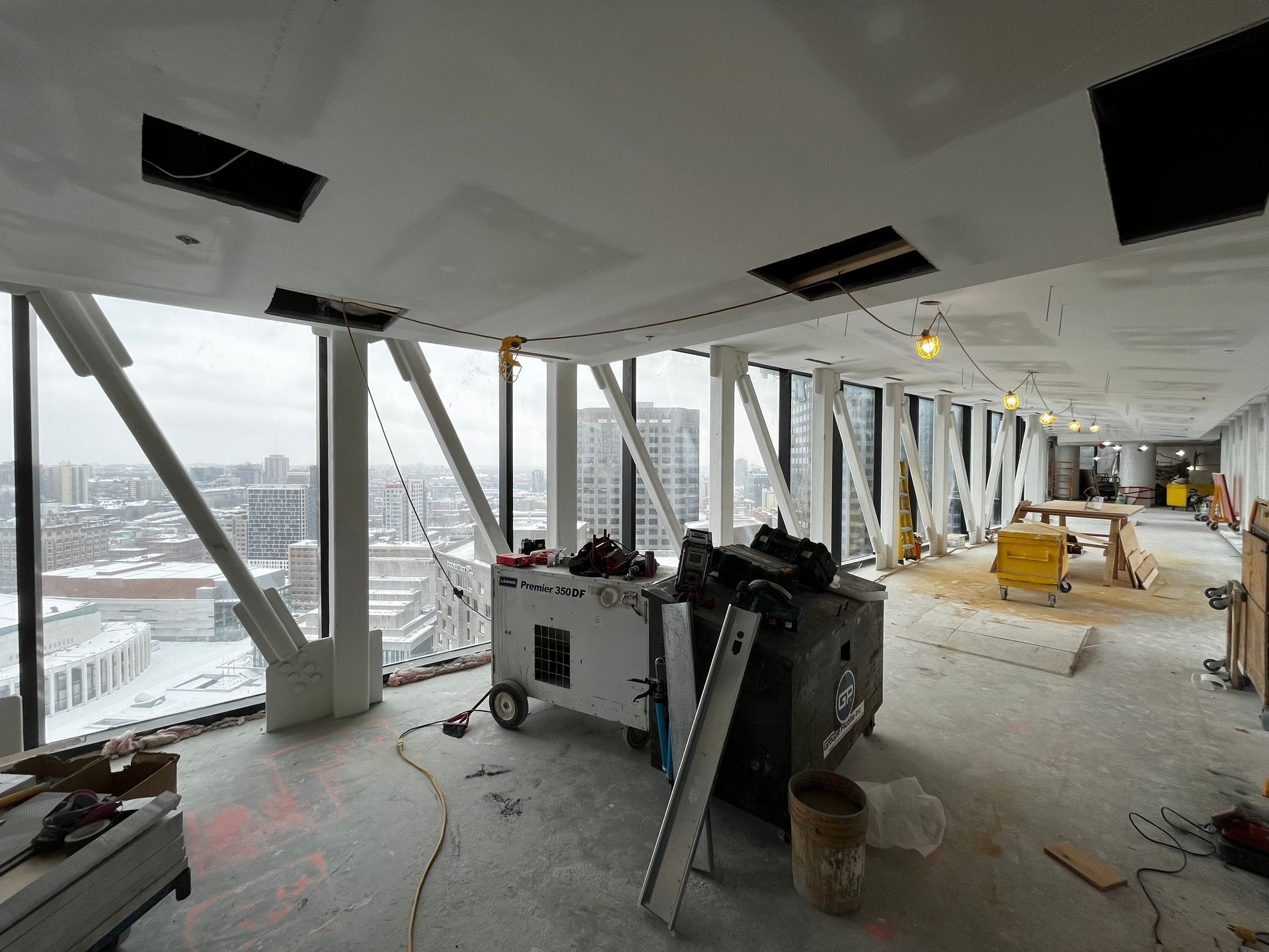 Intérieur d'un chantier de construction avec de grandes fenêtres, des poutres apparentes, des équipements et une vue sur la ville.