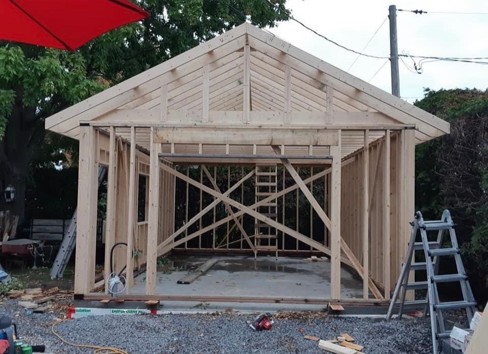 Abri en bois en construction ; charpente terminée, chevrons en place. À l’extérieur, éclairage naturel.