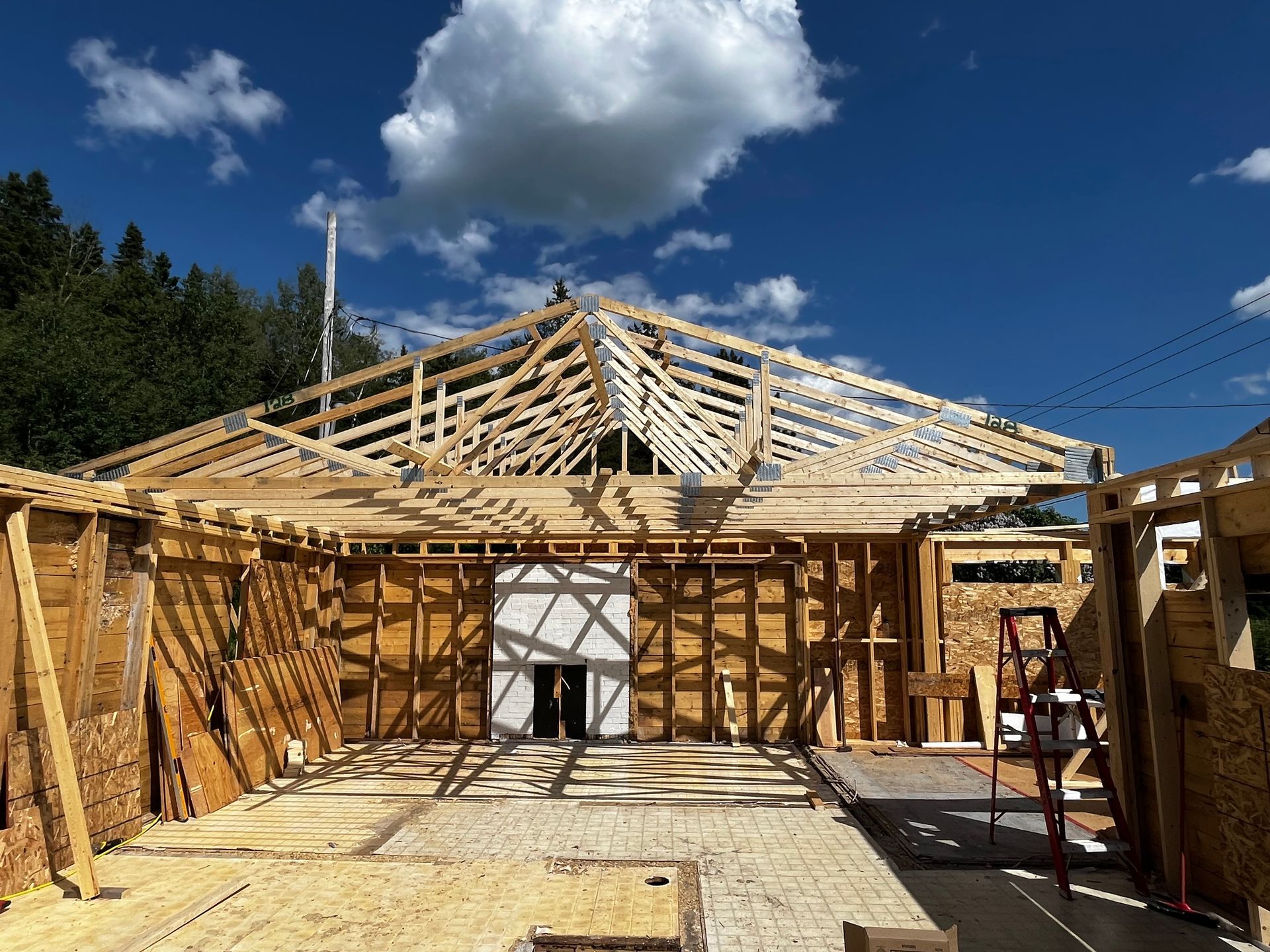 Chantier de construction : charpente en bois d'un bâtiment avec fermes de toit sur fond de ciel bleu.