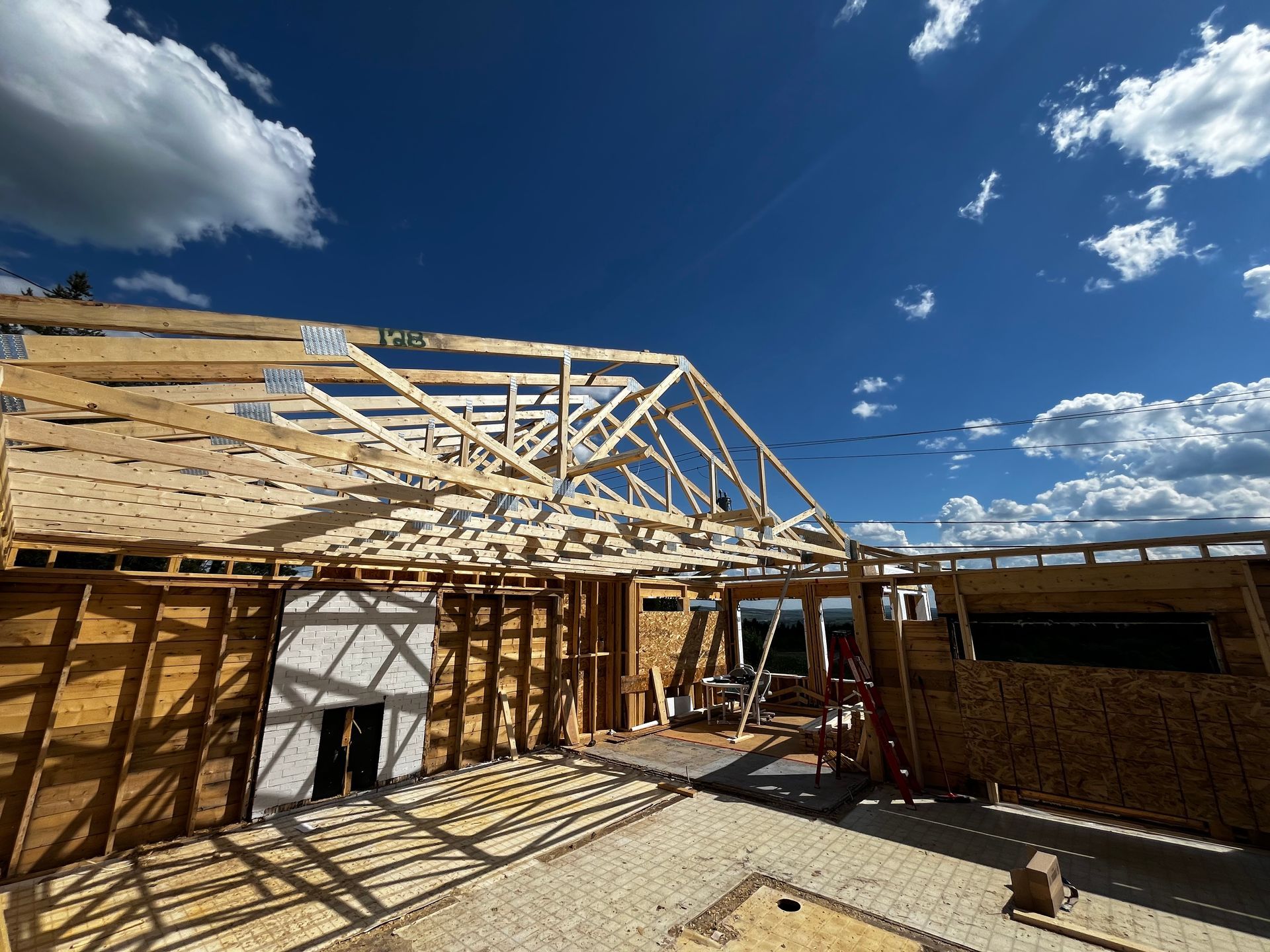 Construction d'une maison à ossature bois apparente sous un ciel bleu nuageux.
