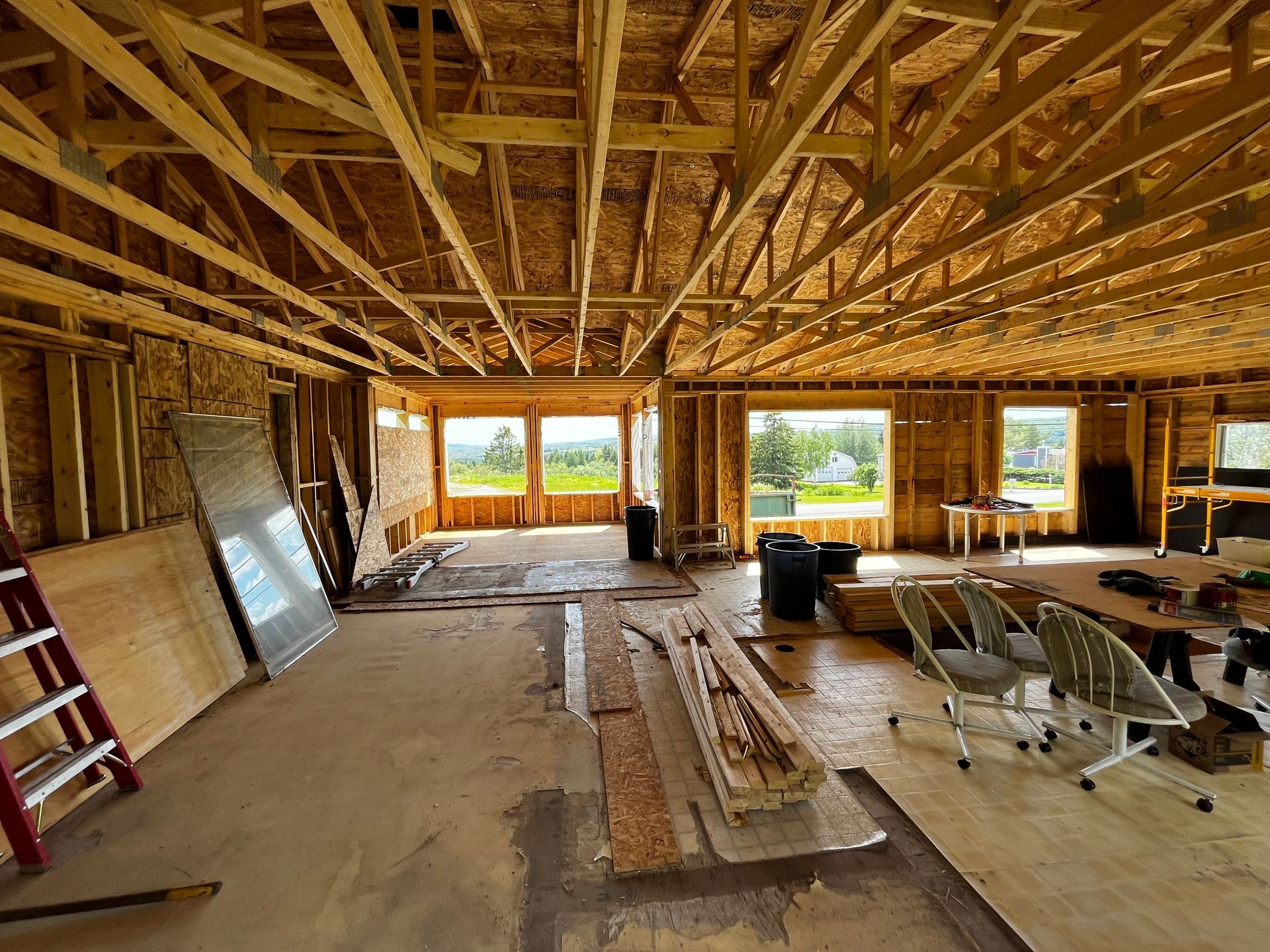 Intérieur d'une maison en construction ; poutres et montants en bois apparents, fenêtres ouvertes donnant sur le paysage.