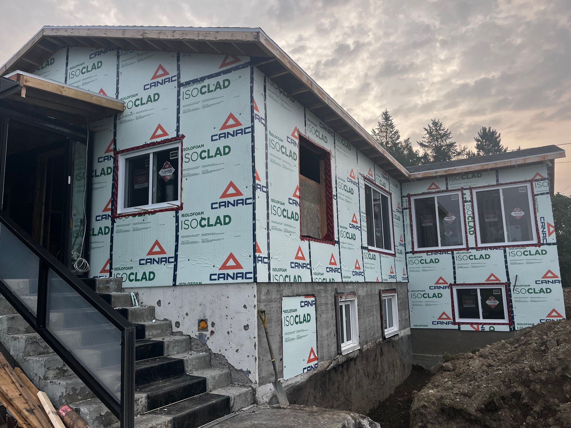 Maison en construction avec isolation bleue, fenêtres et fondations en béton. Vue extérieure.