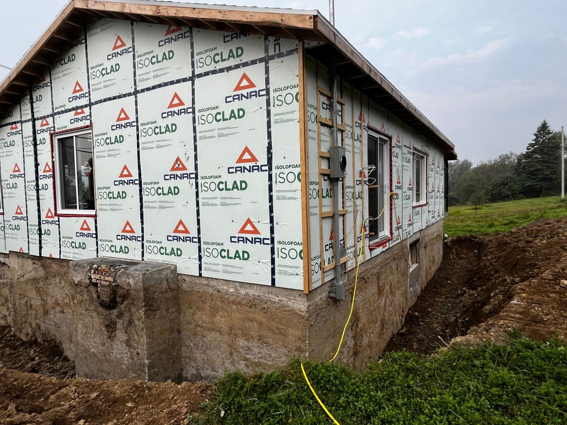 Maison en construction avec revêtement Poclad et fondations en béton non finies.