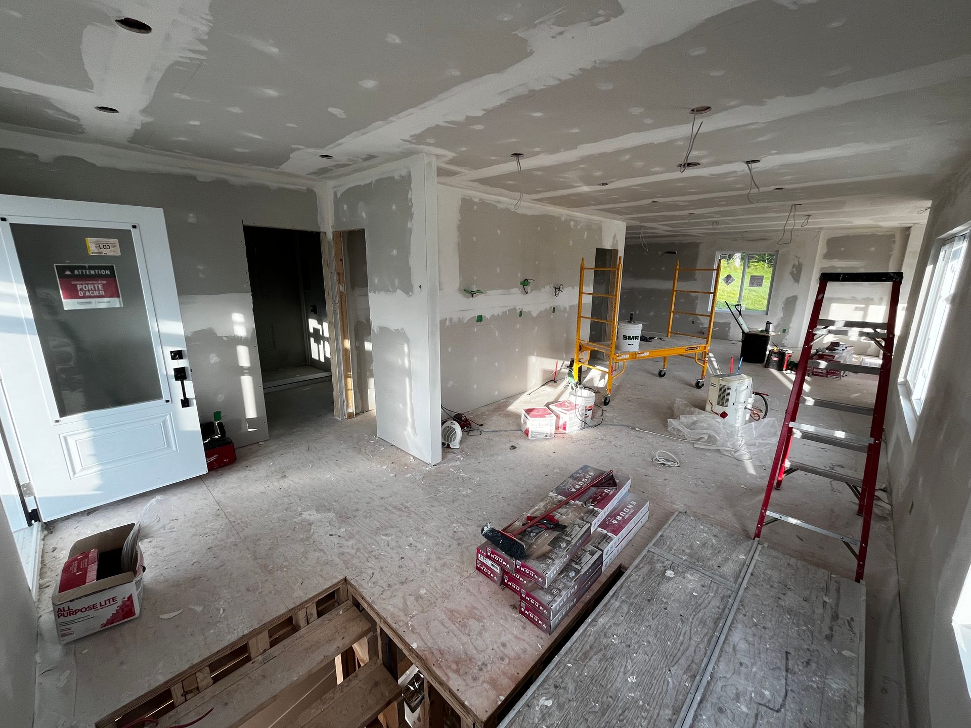 Scène de construction intérieure avec cloisons sèches et outils ; porte, murs non finis, échelle, échafaudage.