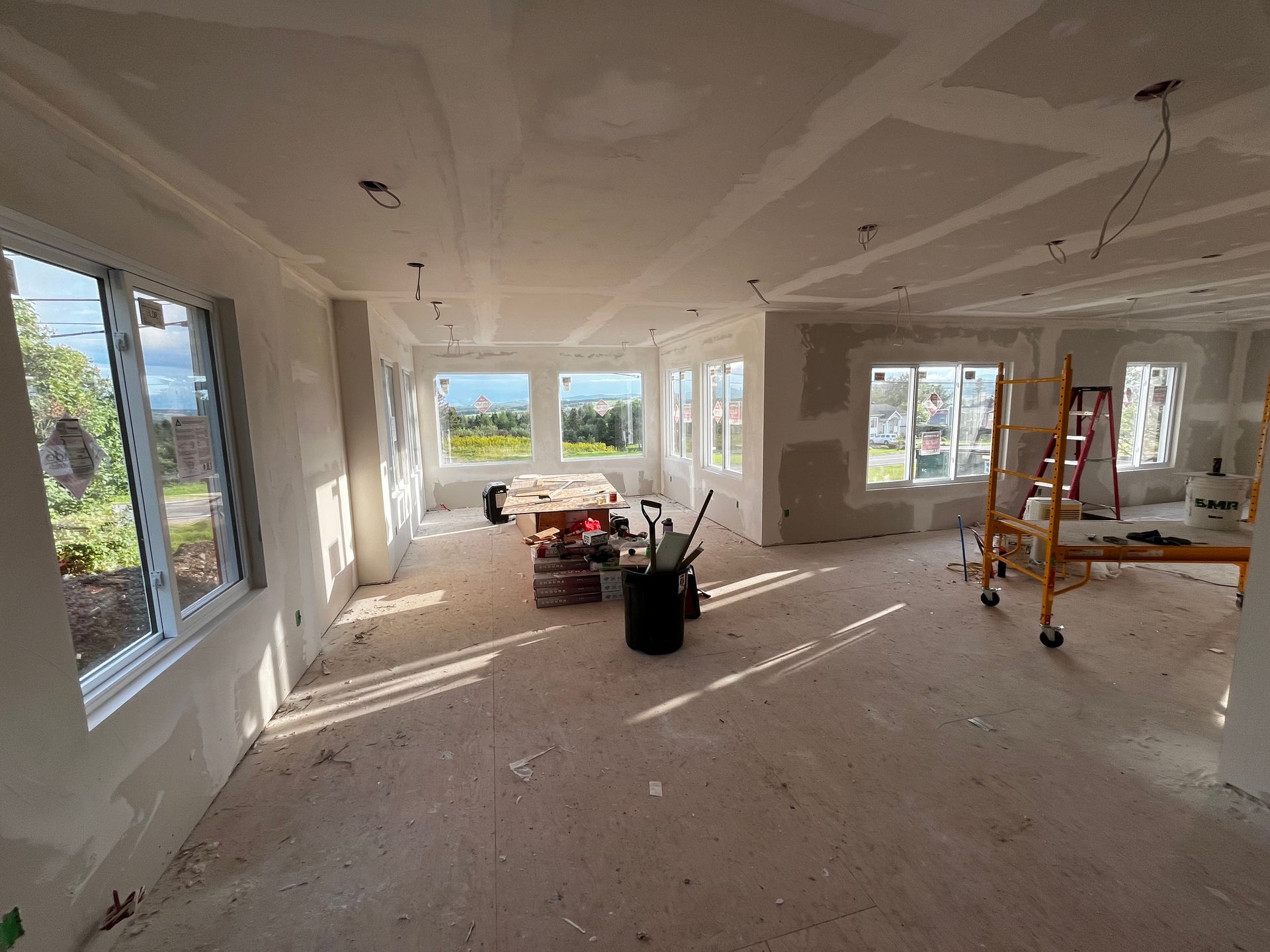 Intérieur d'une pièce en construction avec des cloisons sèches et de nombreuses fenêtres, des outils de construction sont éparpillés.