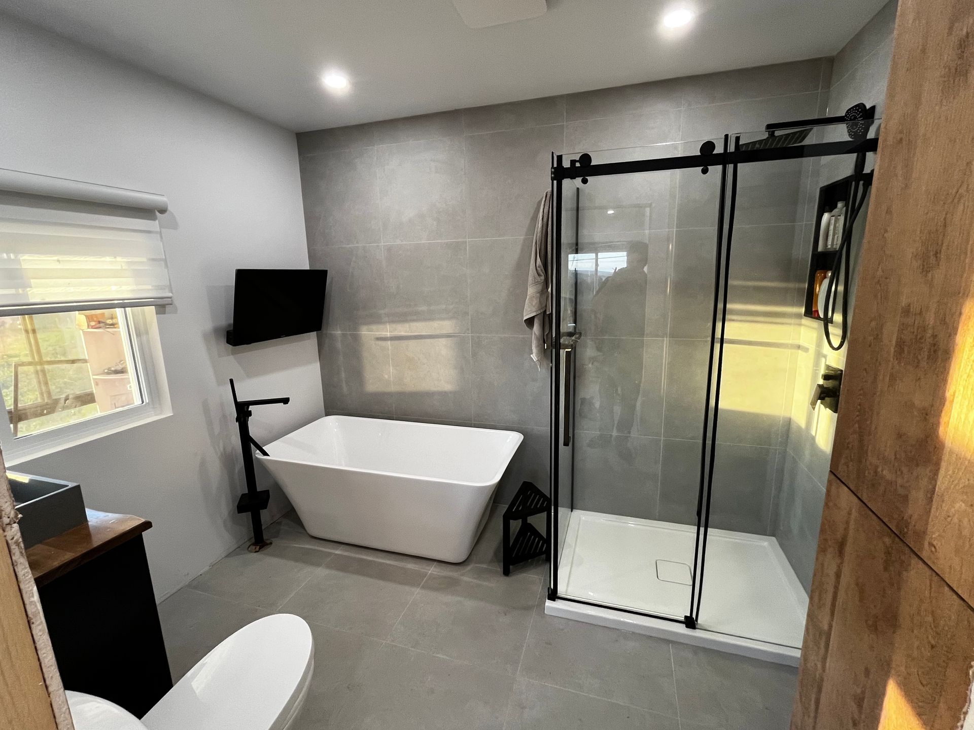 Salle de bains moderne avec carrelage gris, baignoire îlot et douche en verre.