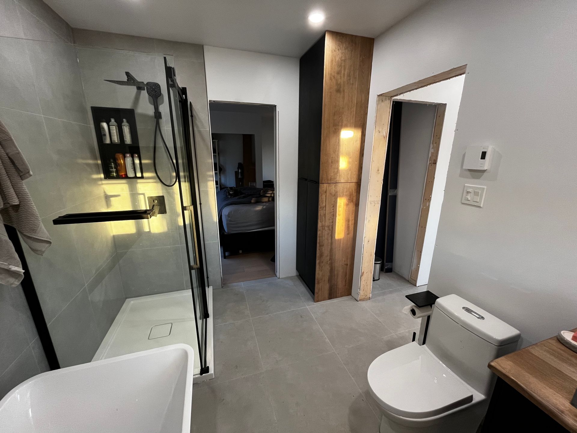 Salle de bains moderne avec douche, toilettes et meuble-lavabo. Tons neutres, mur d'accent en bois.