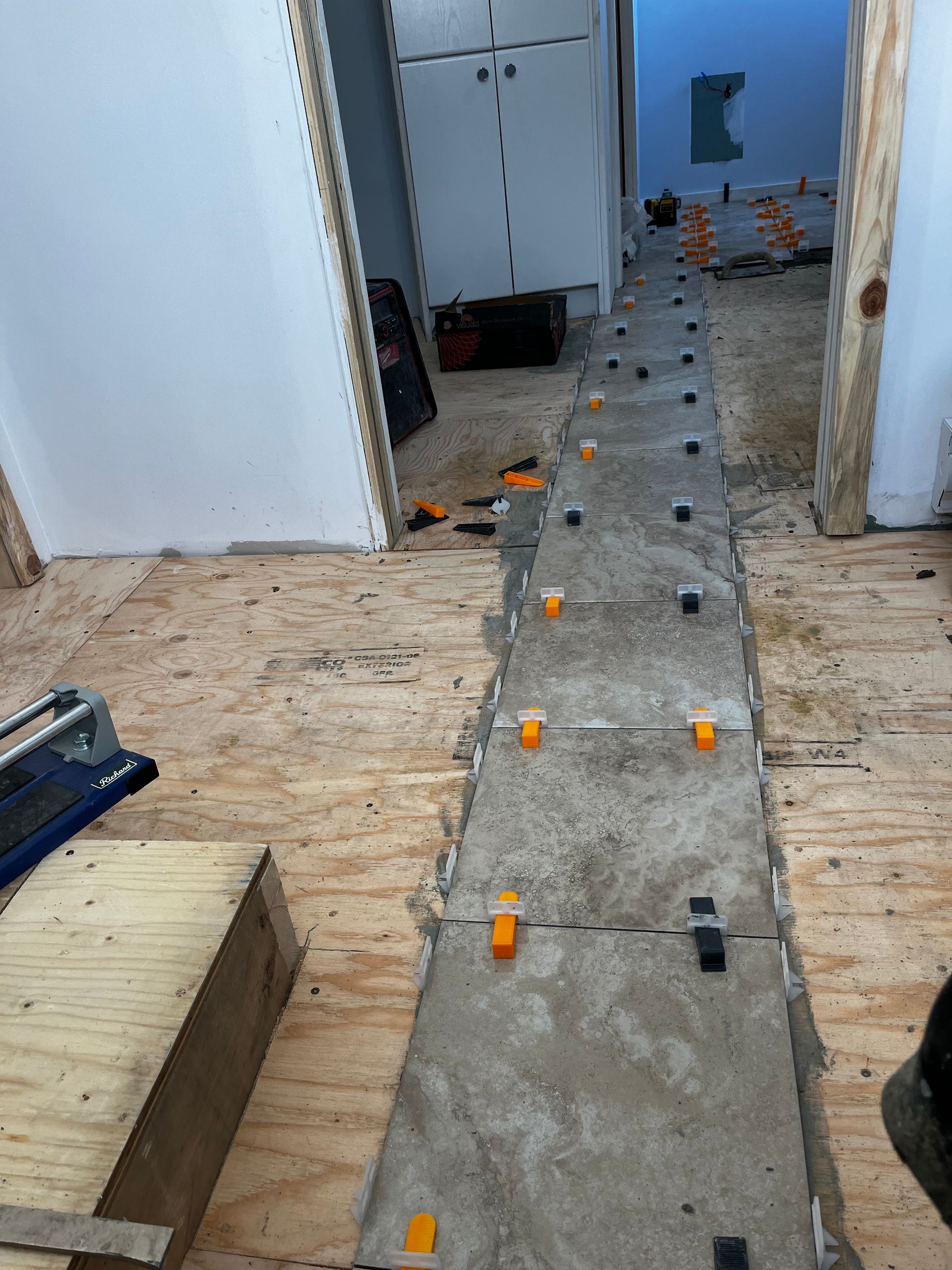 Pose de carrelage en cours. Carrelage posé avec des clips de nivellement dans un couloir. Sol en contreplaqué, murs blancs.