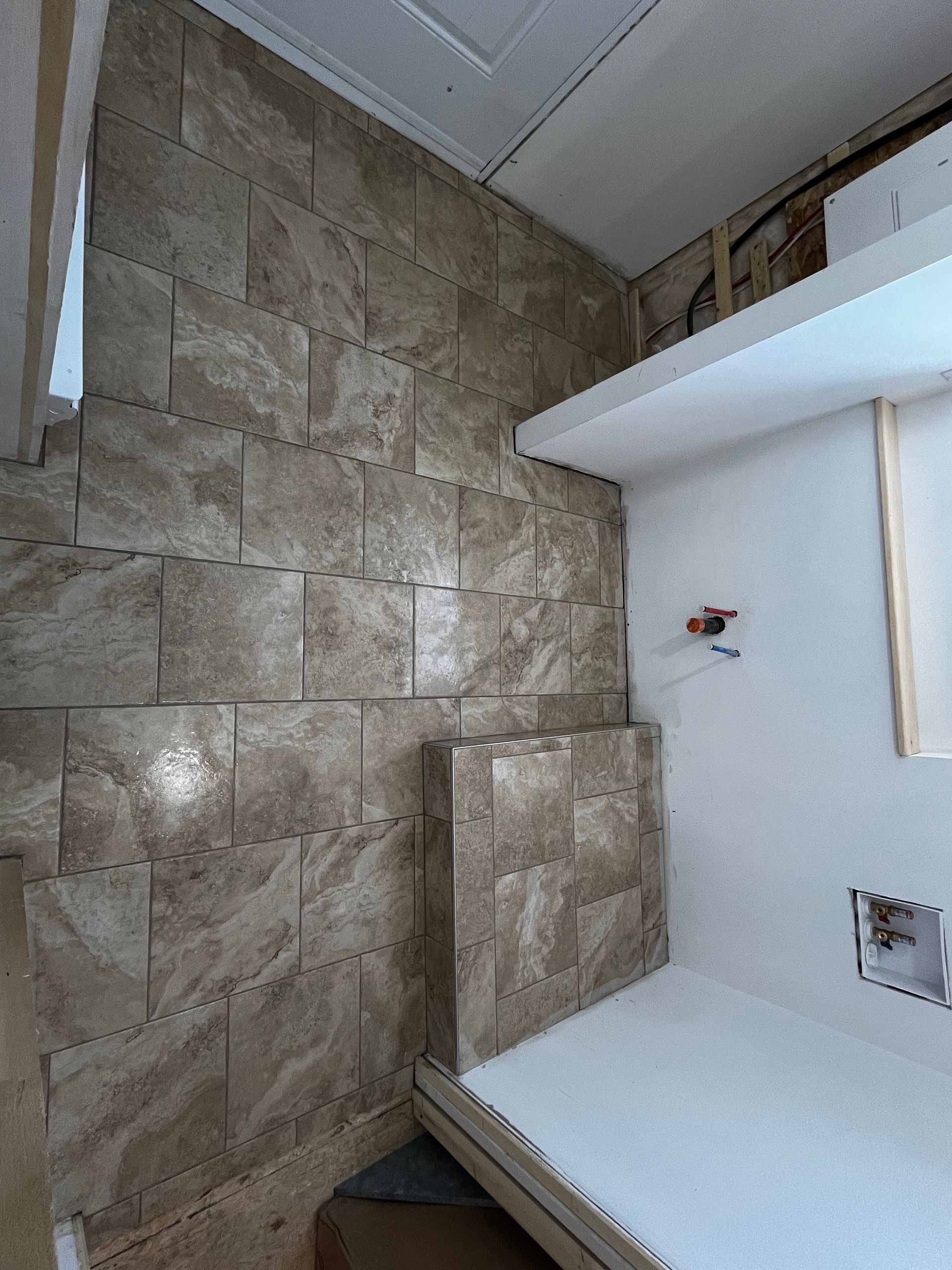 Mur carrelé et étagère dans la salle de bain. Carrelage beige, étagère blanche, mur brut.