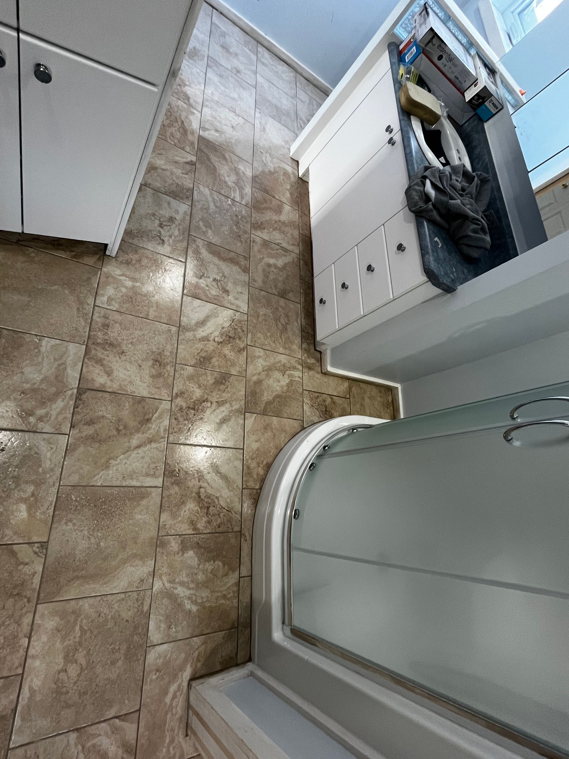 Salle de bains avec murs et sol carrelés de beige, meuble blanc et douche avec porte en verre.