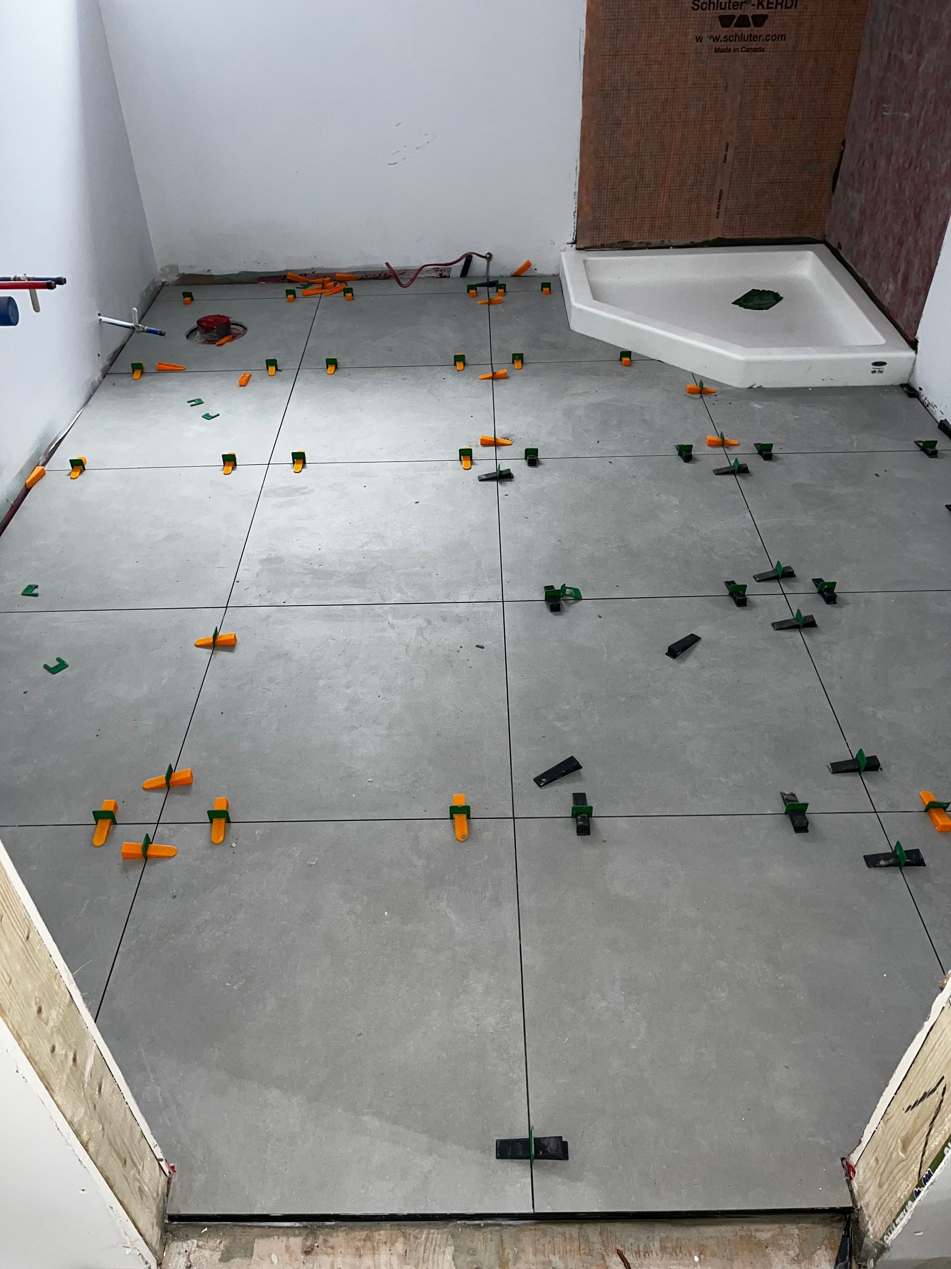 Le sol de la salle de bain est carrelé avec des carreaux gris, des clips de nivellement et des entretoises. Le receveur de douche est installé dans un angle.