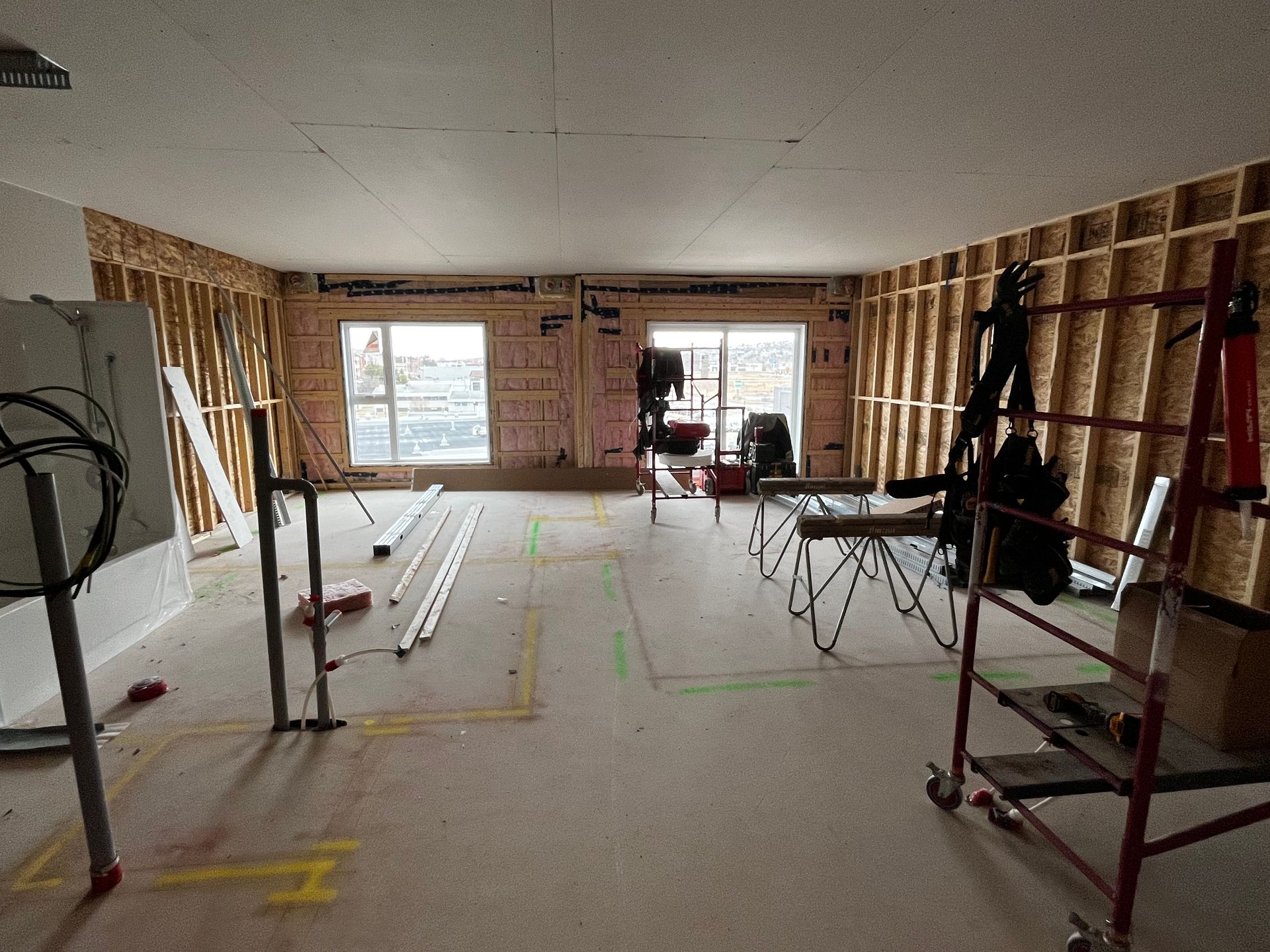 Intérieur d'une pièce en construction, avec des montants en bois apparents, des fenêtres et des outils.