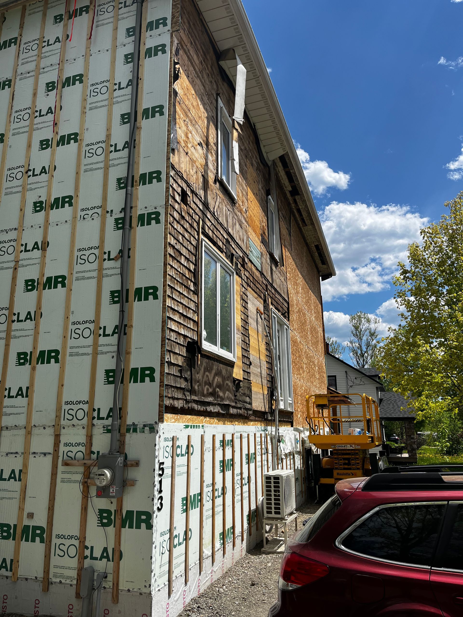 Façade du bâtiment en construction ; briques et isolation apparentes ; journée ensoleillée.