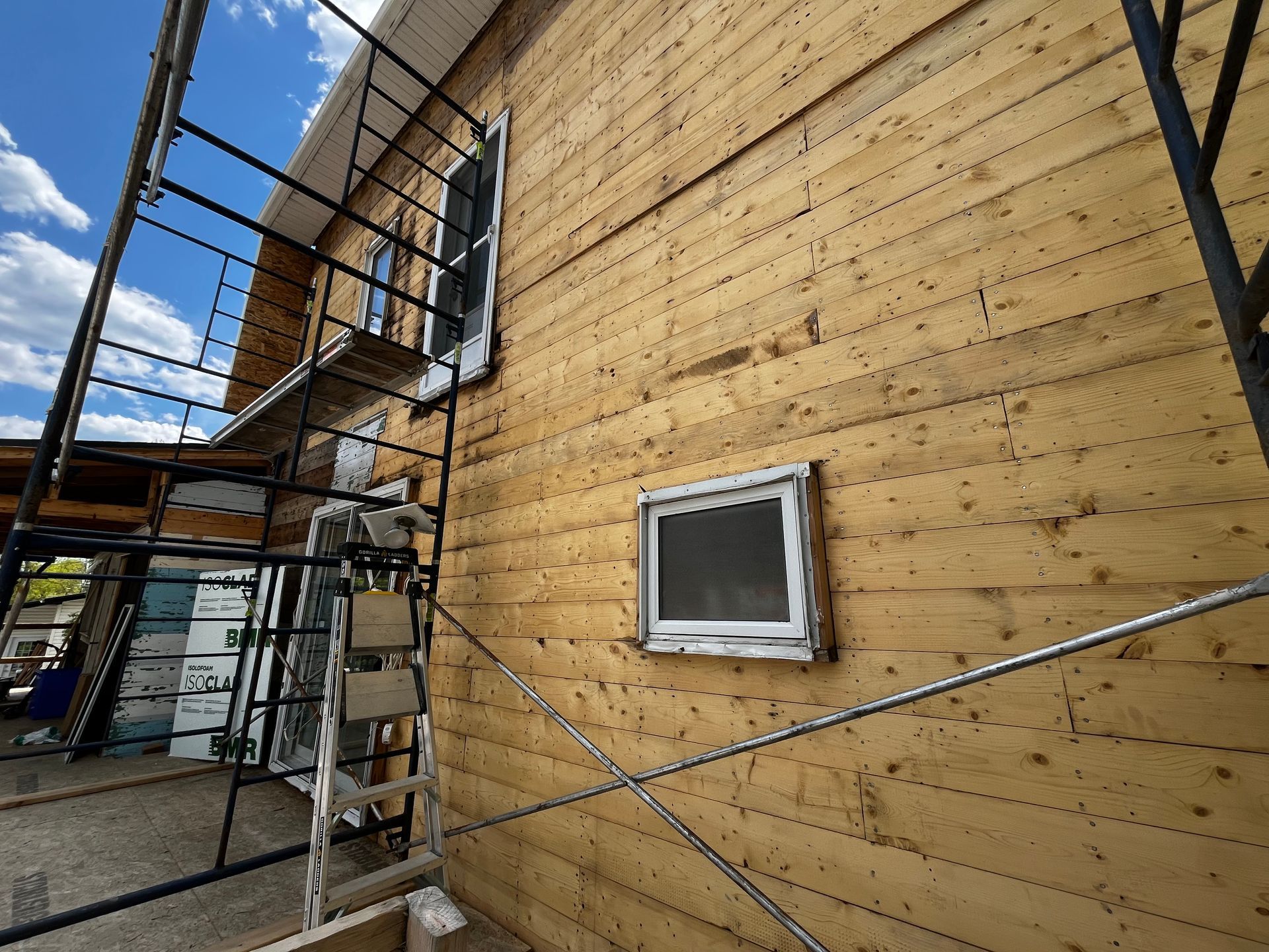 Façade du bâtiment avec bardage en bois inachevé et échafaudages. Petite fenêtre visible.