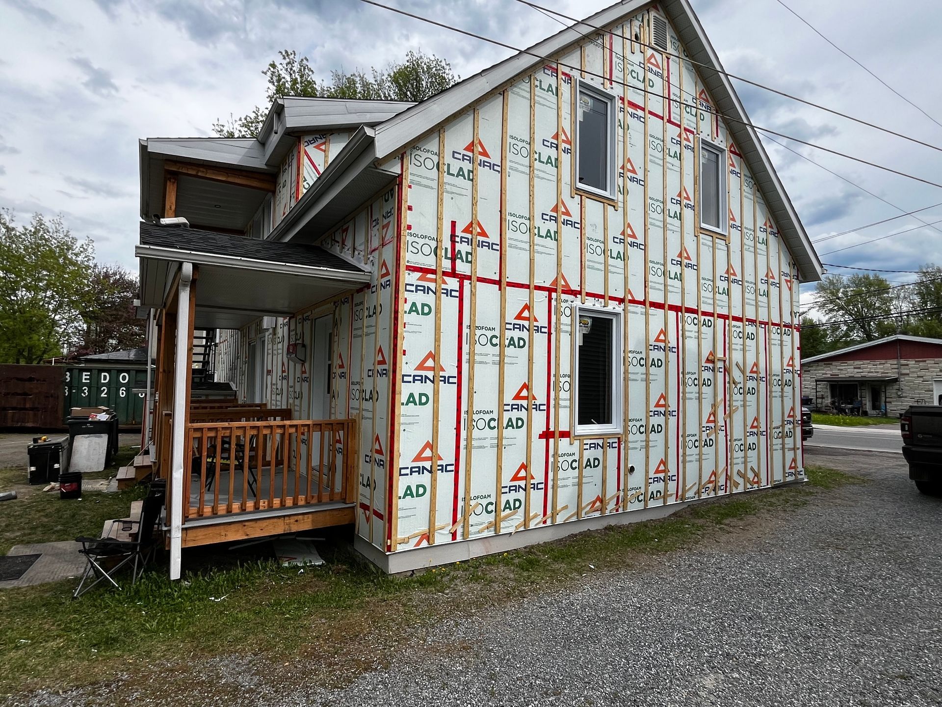 Façade d'une maison en construction, le revêtement est apparent. On distingue des tons blancs, rouges et boisés. Ciel gris.