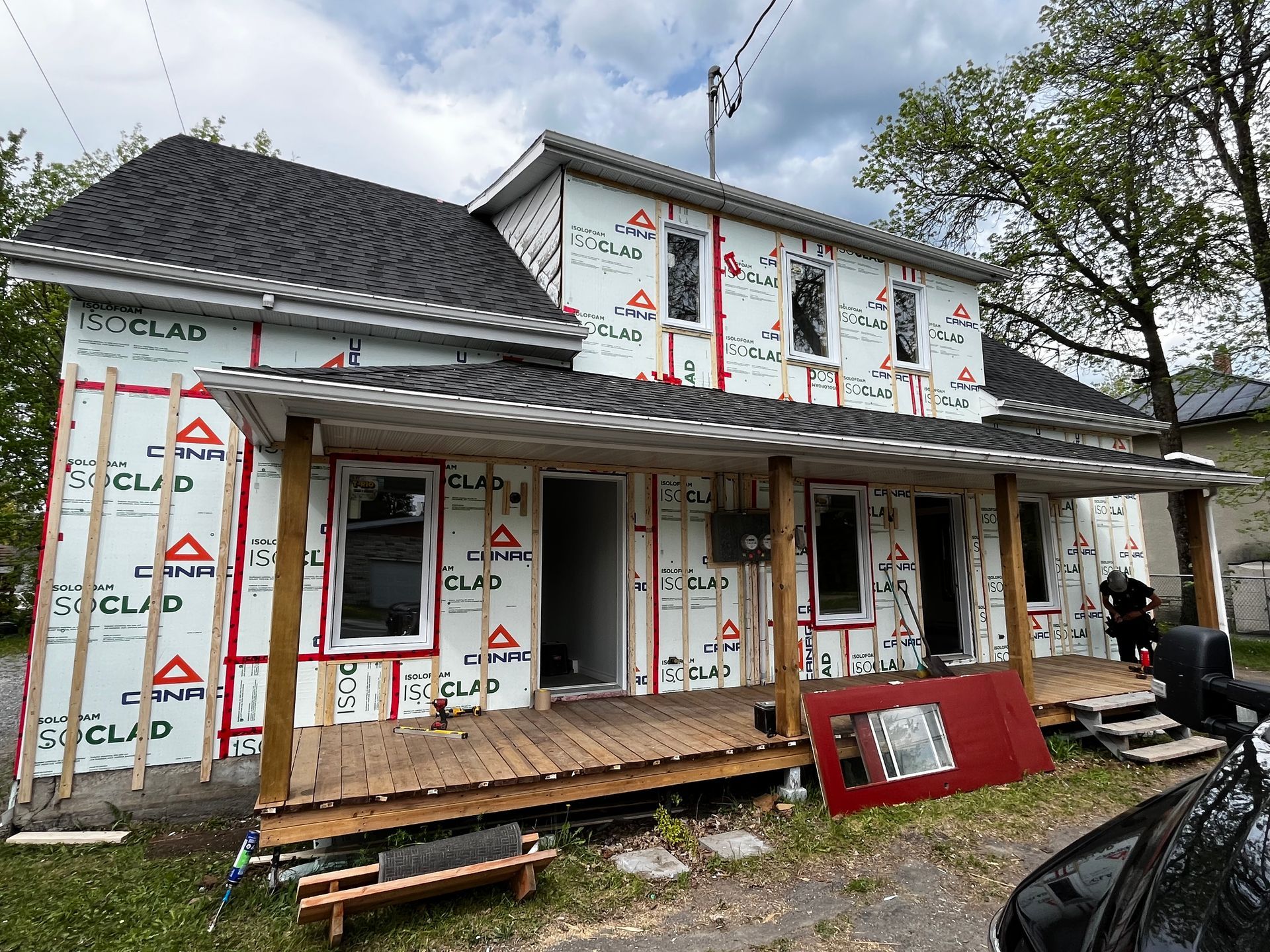 Façade de maison en construction, revêtue de bardage blanc et rouge, avec un porche en bois.