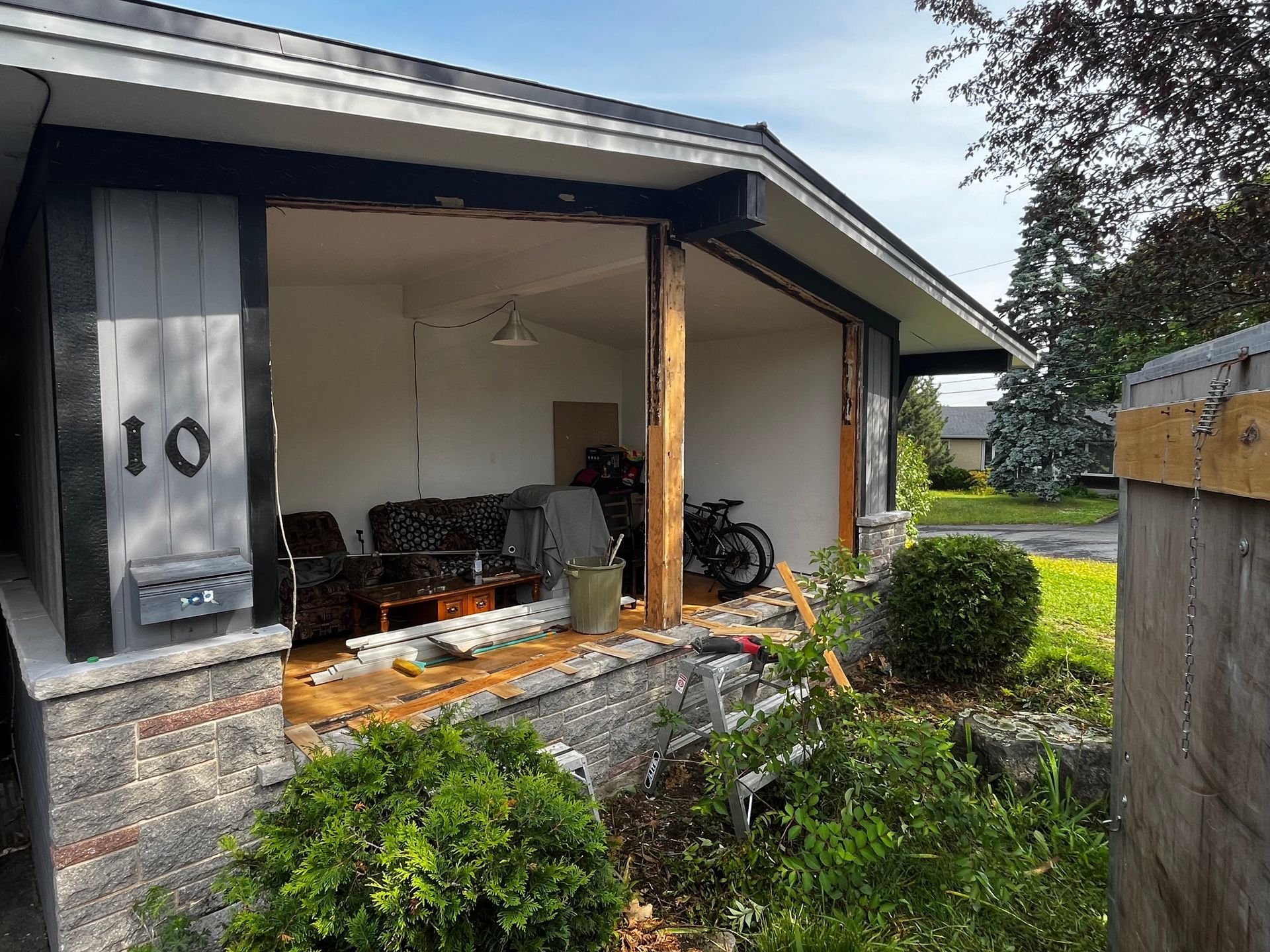 Extérieur d'une maison dont l'entrée a été démolie, laissant apparaître l'intérieur. Débris et meubles sont visibles. Le numéro 10 figure sur la maison.