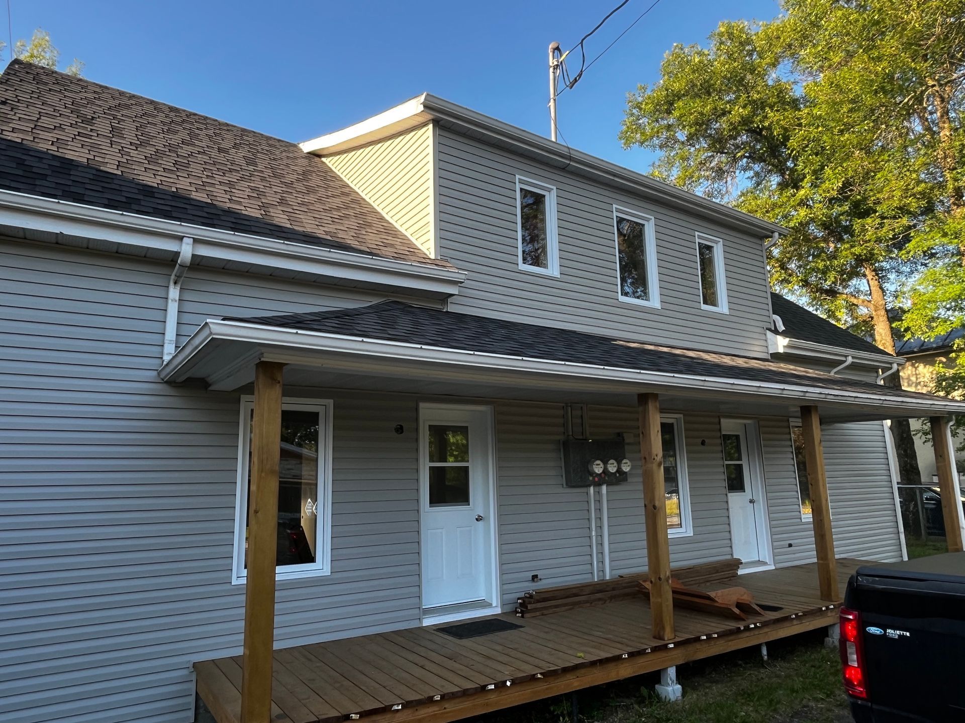 Bâtiment de deux étages gris clair avec un porche en bois et un toit foncé.
