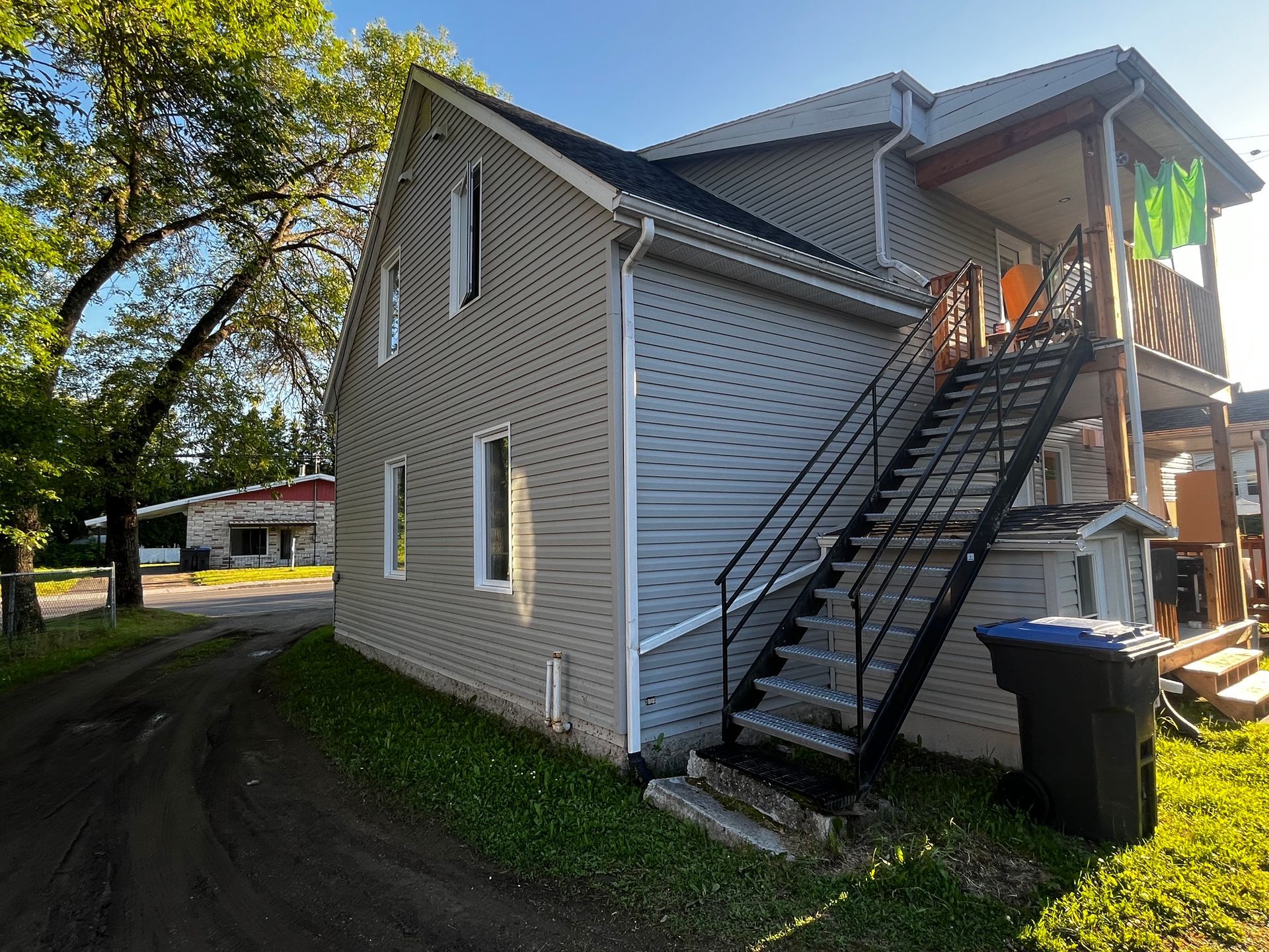 Bâtiment gris de deux étages avec escalier extérieur et porche noirs. Pelouse verte et allée de gravier.