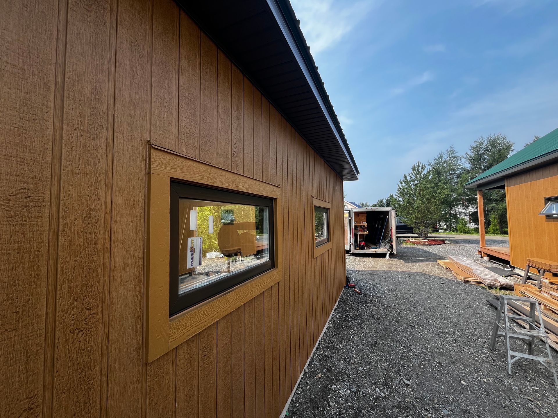 Bâtiment aux murs bruns avec des fenêtres sous un ciel bleu, sur un sol de gravier.