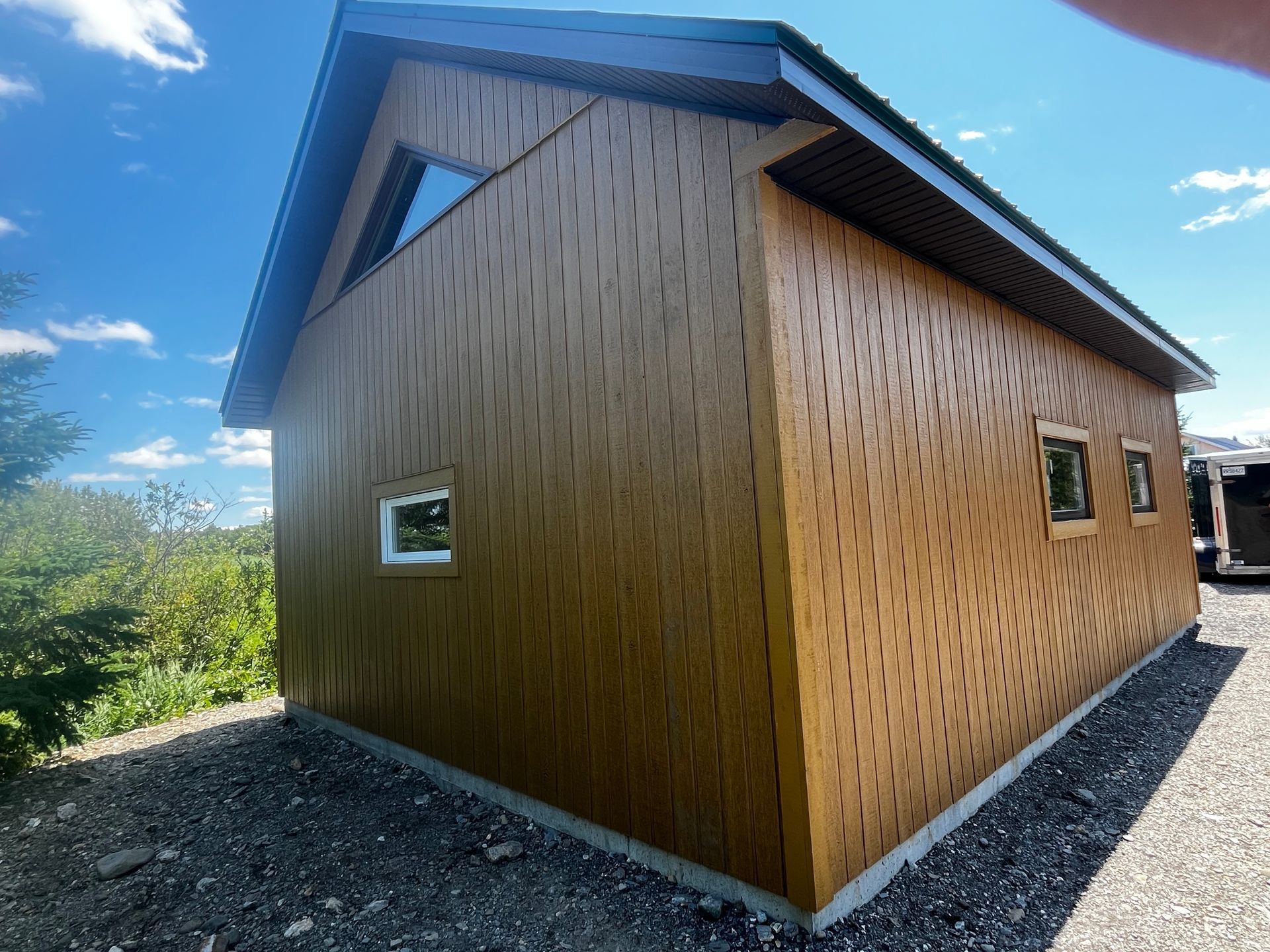 Bâtiment aux boiseries brunes et aux motifs sculptés originaux. Il comporte une fenêtre triangulaire et deux fenêtres rectangulaires. Il est situé sur un sol gravillonné.