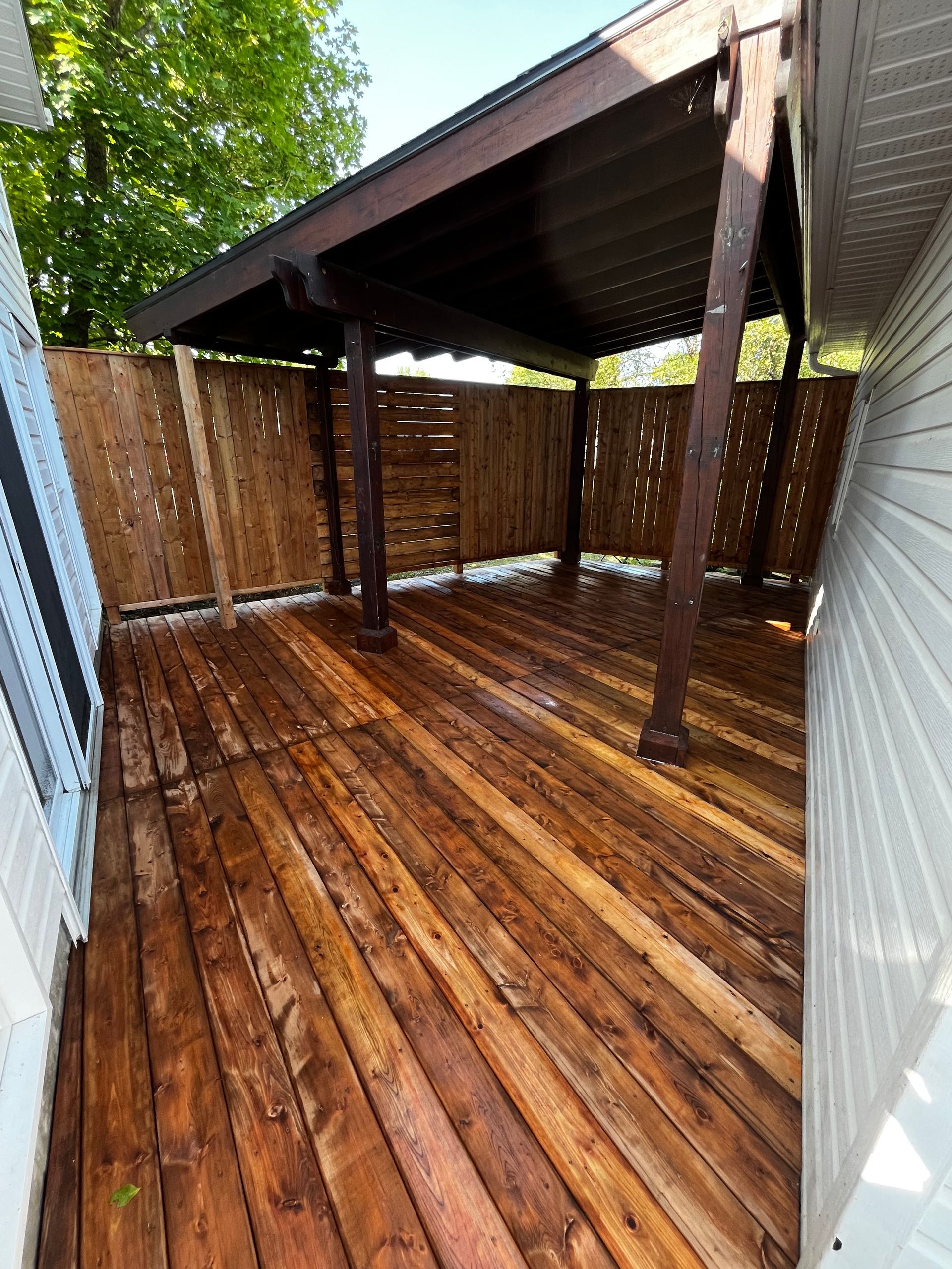 Terrasse en bois avec pergola brun foncé et clôture d'intimité, entourée par le revêtement de la maison.