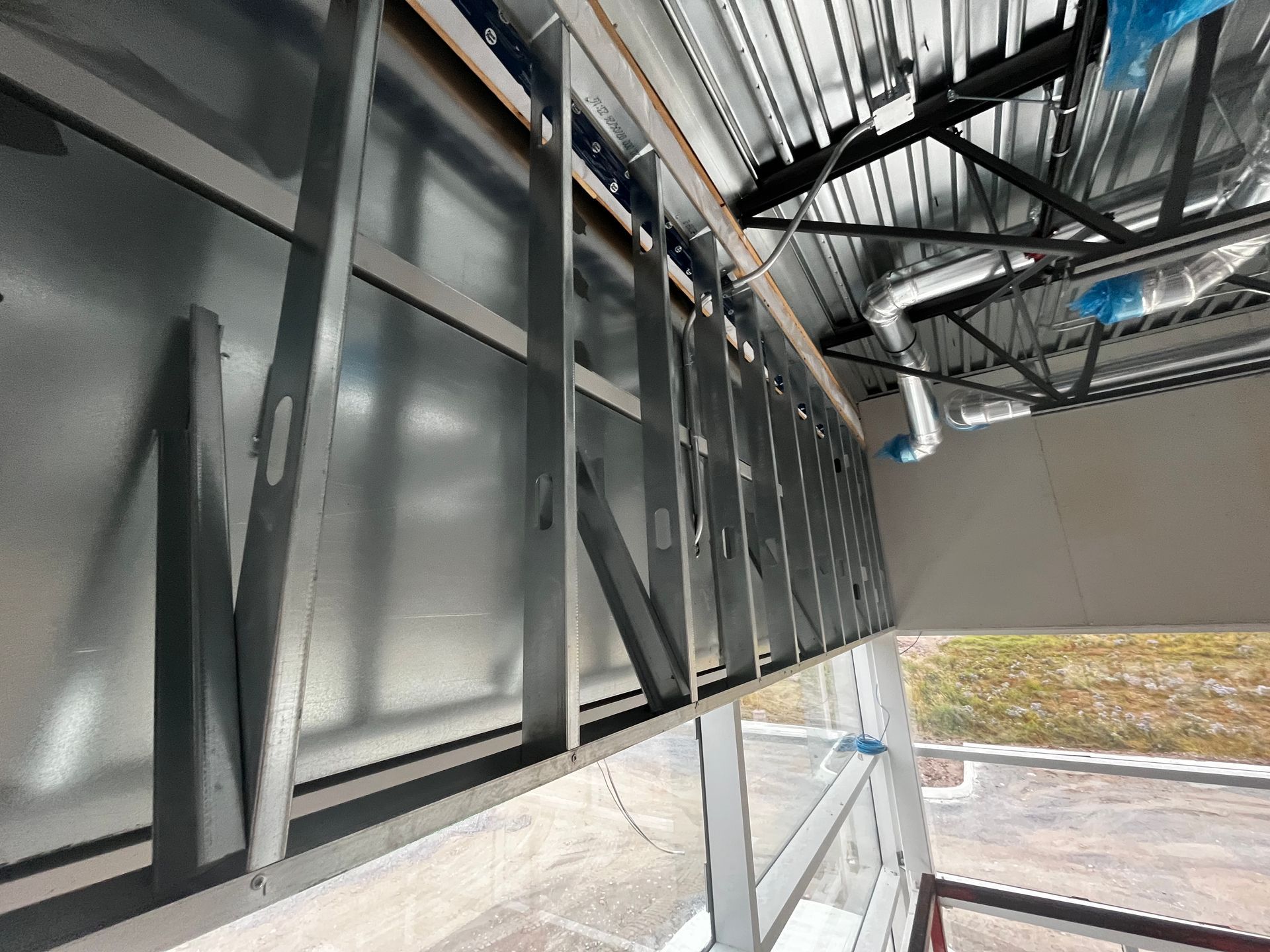 Charpente métallique contre un mur métallique avec une fenêtre en dessous et un plafond apparent, chantier de construction.