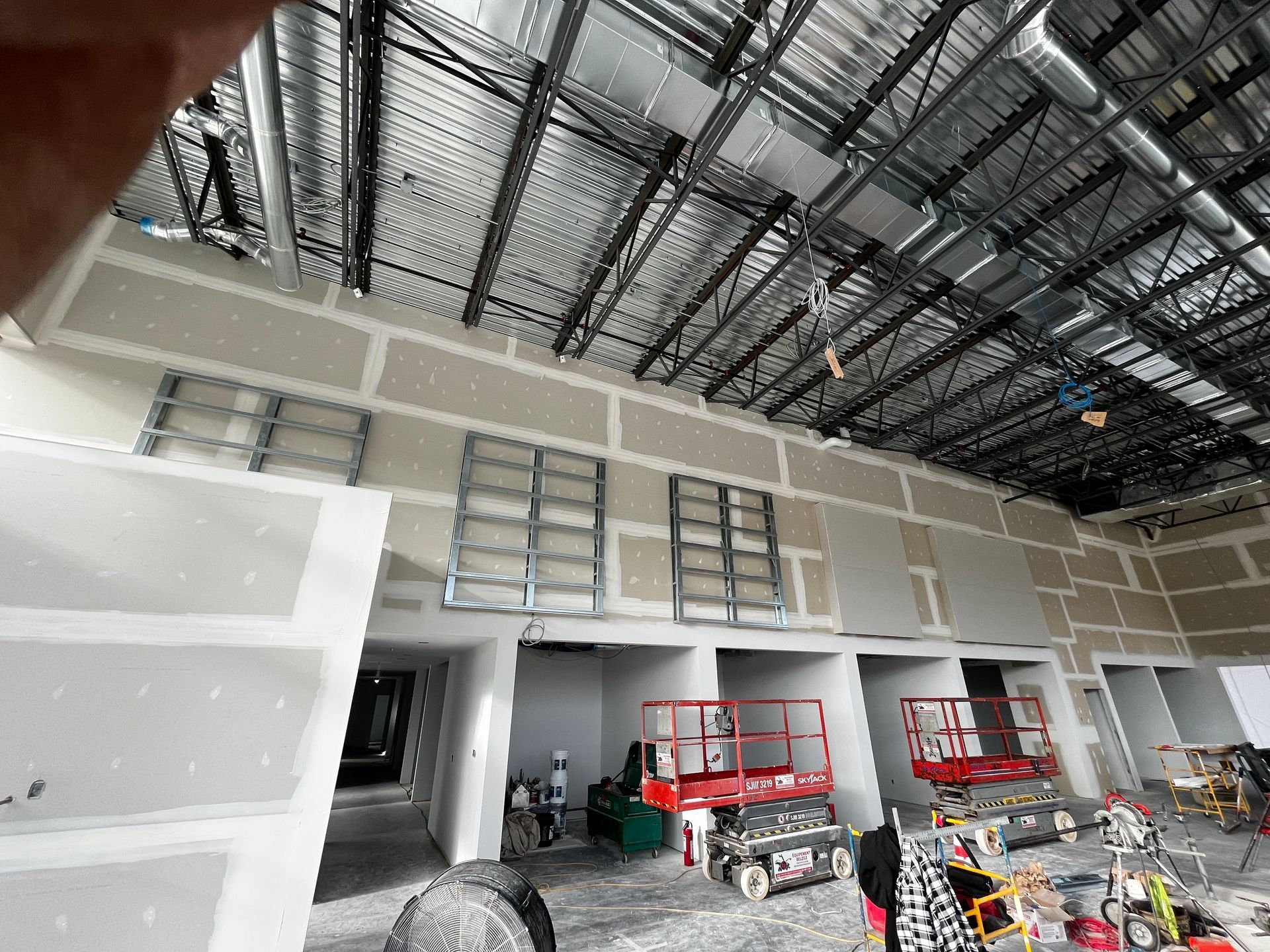 Travaux de construction dans un bâtiment, montrant la pose de cloisons sèches, des nacelles élévatrices et la structure apparente du plafond.