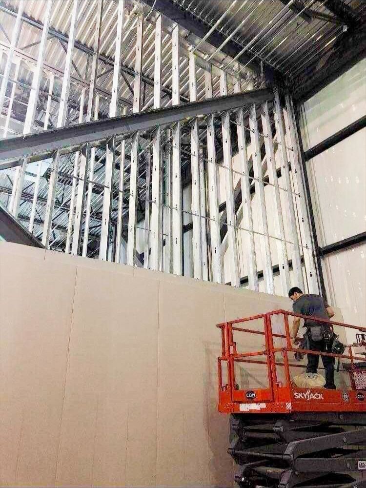 Un homme sur une nacelle installe des panneaux muraux dans un bâtiment en construction.