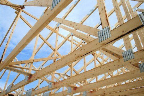 Des charpentes de toit en bois sont en cours de construction sur fond de ciel bleu, reliées par des plaques métalliques.