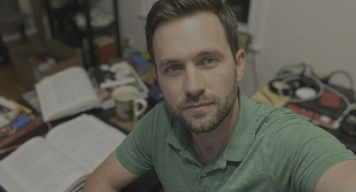 Man in green polo takes a selfie at a cluttered desk with an open notebook and coffee cup