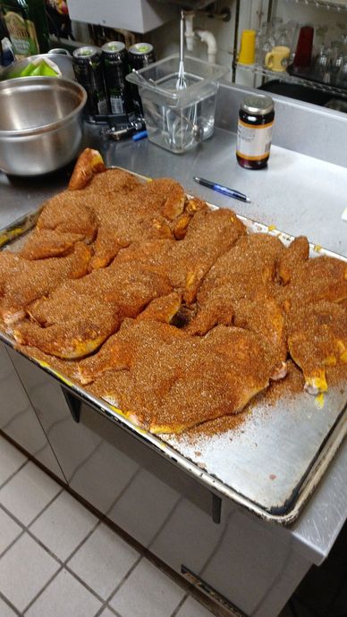 Raw chicken pieces seasoned with spices on a metal tray in a kitchen.