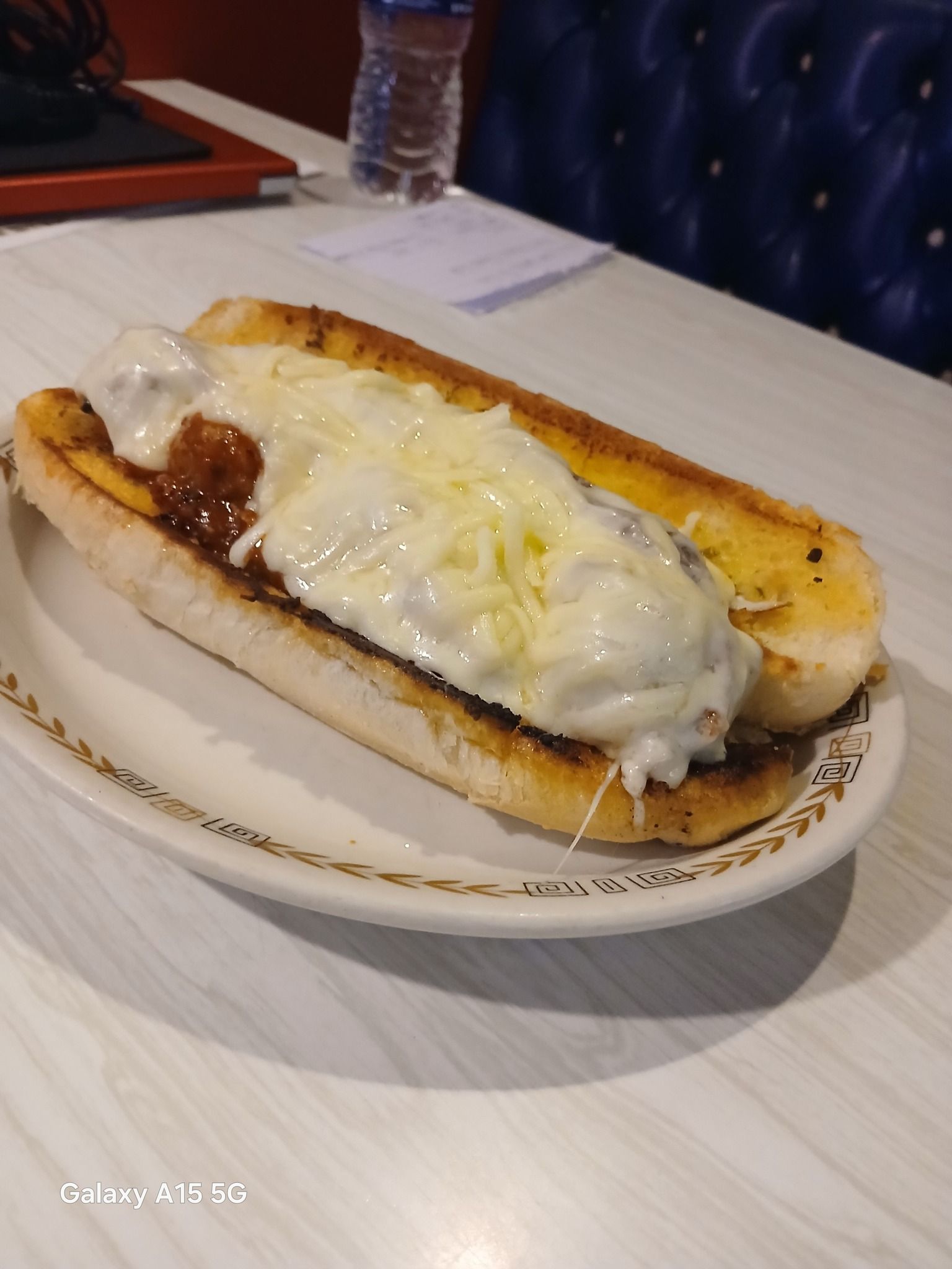 Meatball sub on a white plate, with melted cheese and toasted bread.