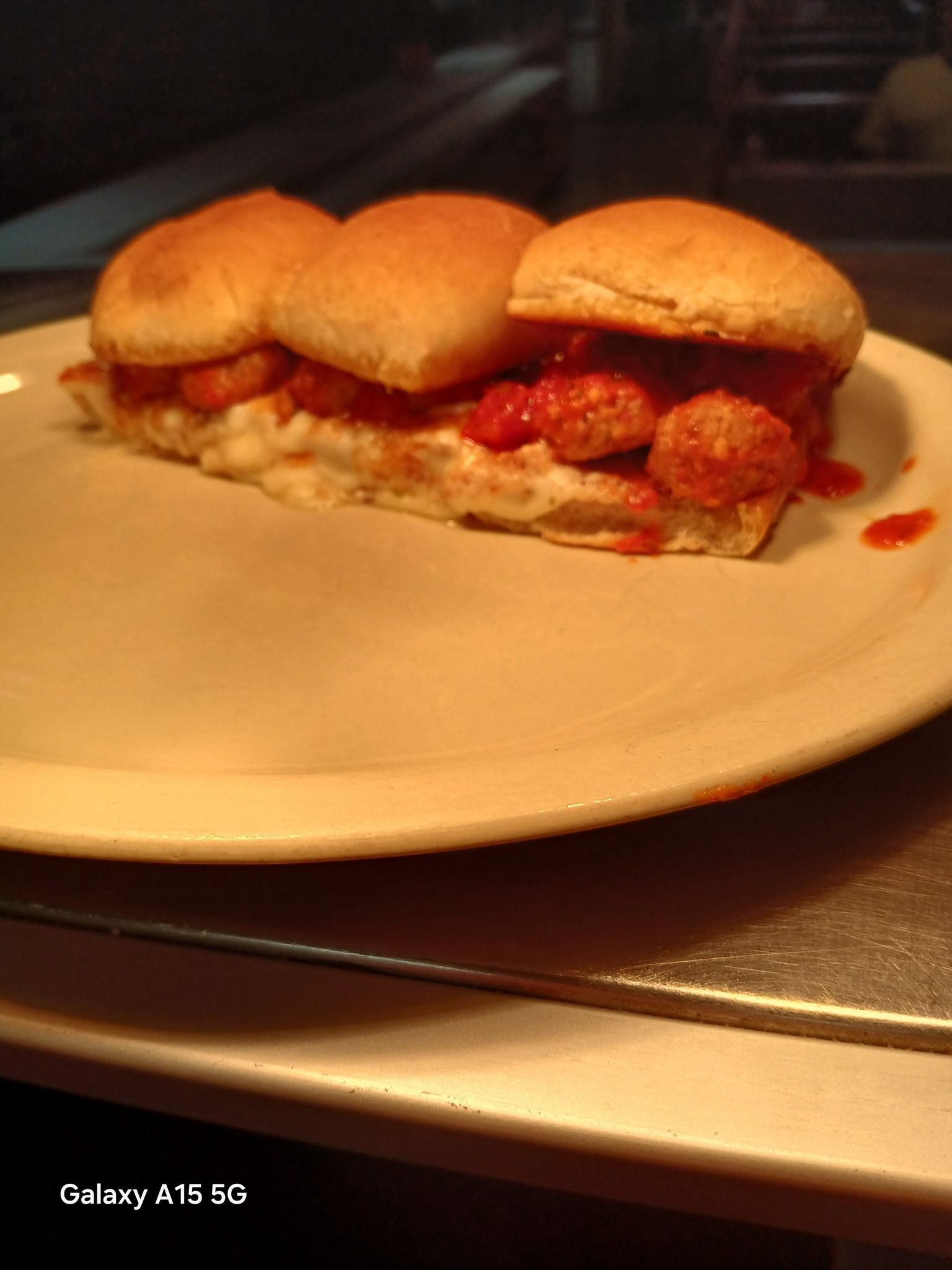 Meatball sandwich on a plate; meatballs covered in sauce, with a roll, on a white plate.