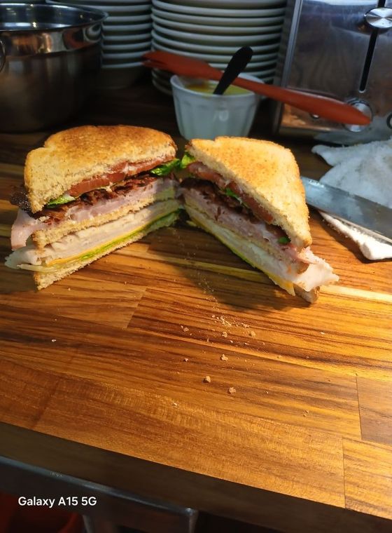 Club sandwich cut in half on a wooden counter, with a white dish and a knife.