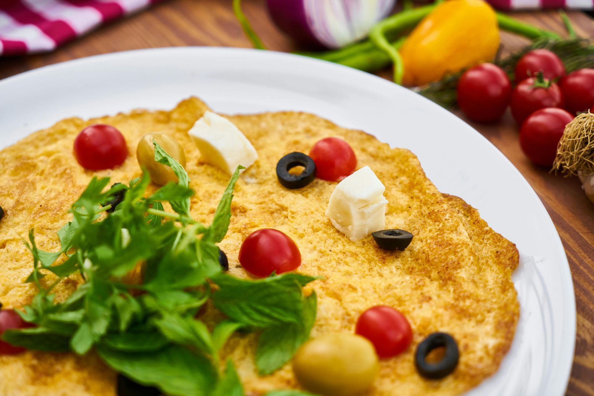 Omelet topped with tomatoes, olives, feta, and greens on a white plate.