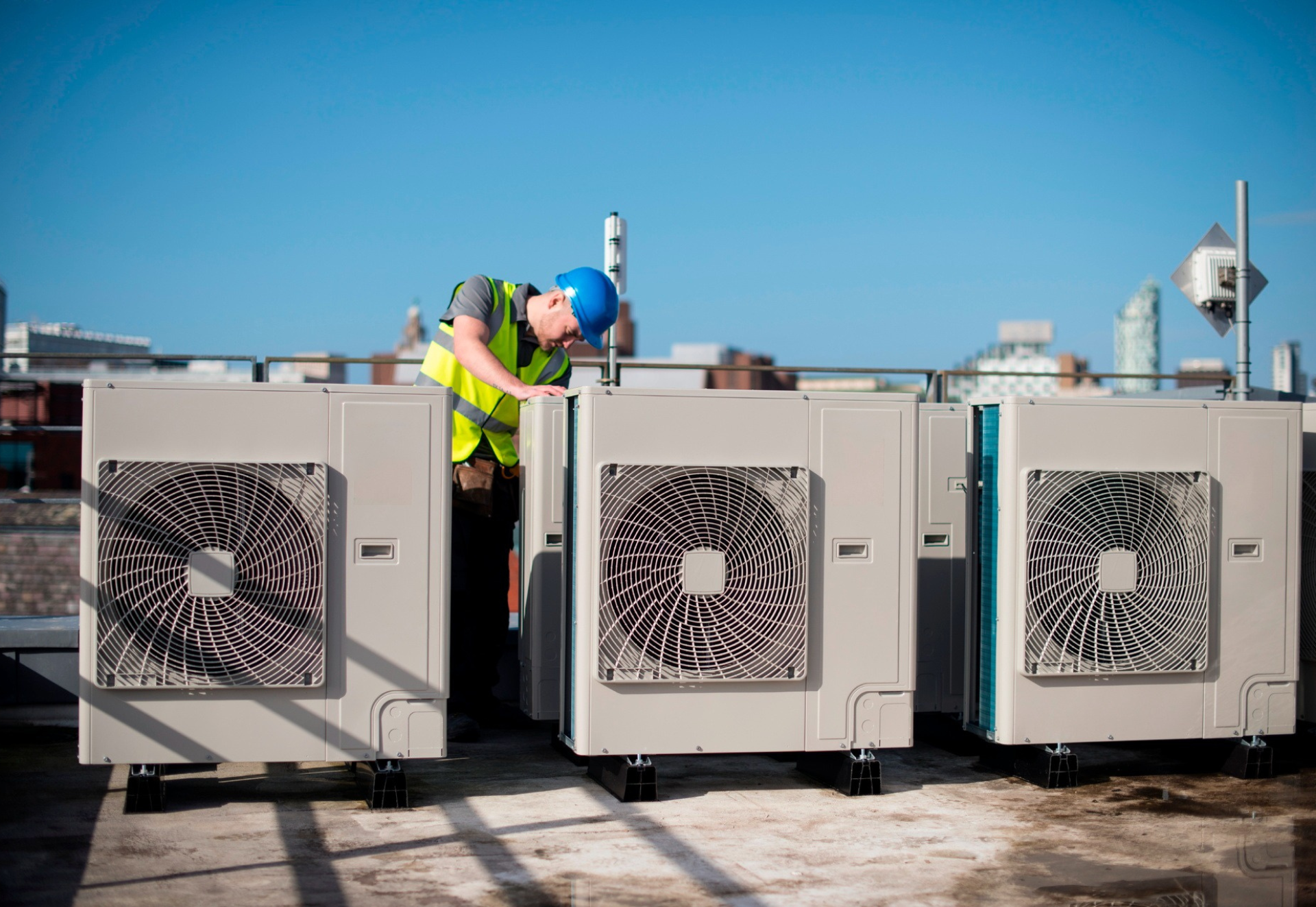 HVAC technician in hard hat and vest inspecting rooftop air conditioning units on a sunny day.