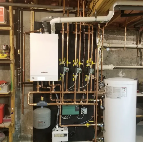 A white boiler is surrounded by copper pipes in a basement