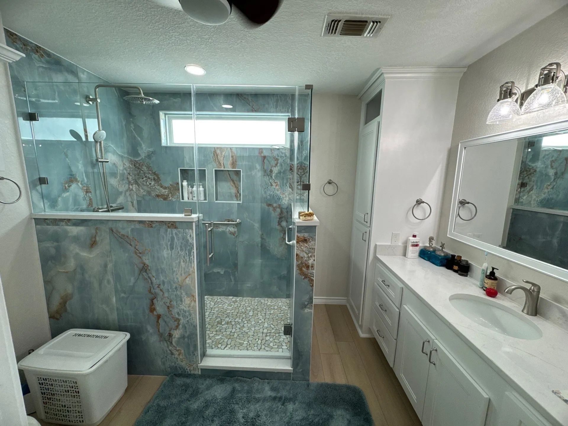 Bright modern bathroom with glass shower, marble tile, and white vanity with double sink.