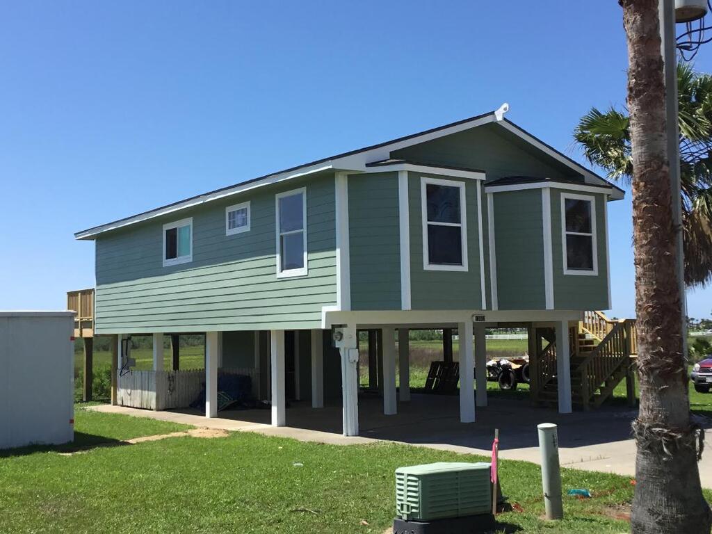 A green house on stilts with a palm tree in front of it