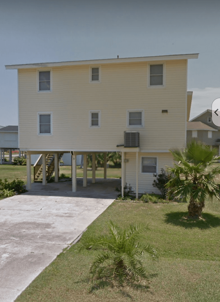 A large white house with a driveway and palm trees in front of it.