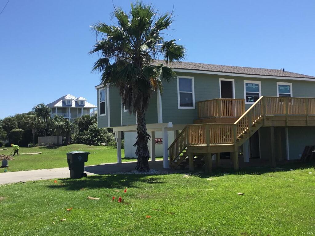 A green house with a wooden deck and stairs is sitting on top of a lush green lawn.