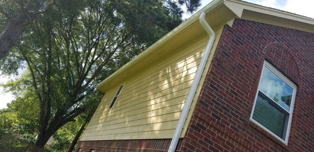 A brick house with a yellow siding and a white gutter