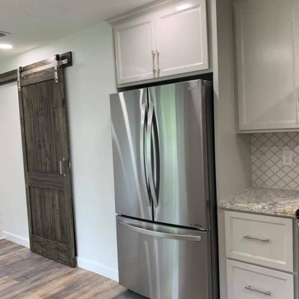 A stainless steel refrigerator is sitting in a kitchen next to a sliding barn door.