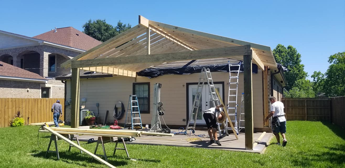 A group of people are working on a wooden structure in front of a house.