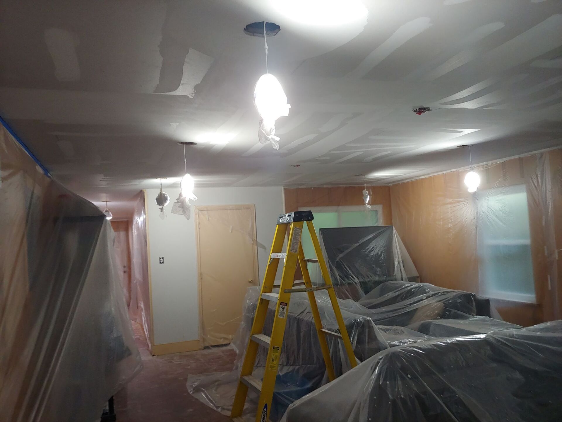 A ladder is sitting in a room covered in plastic.